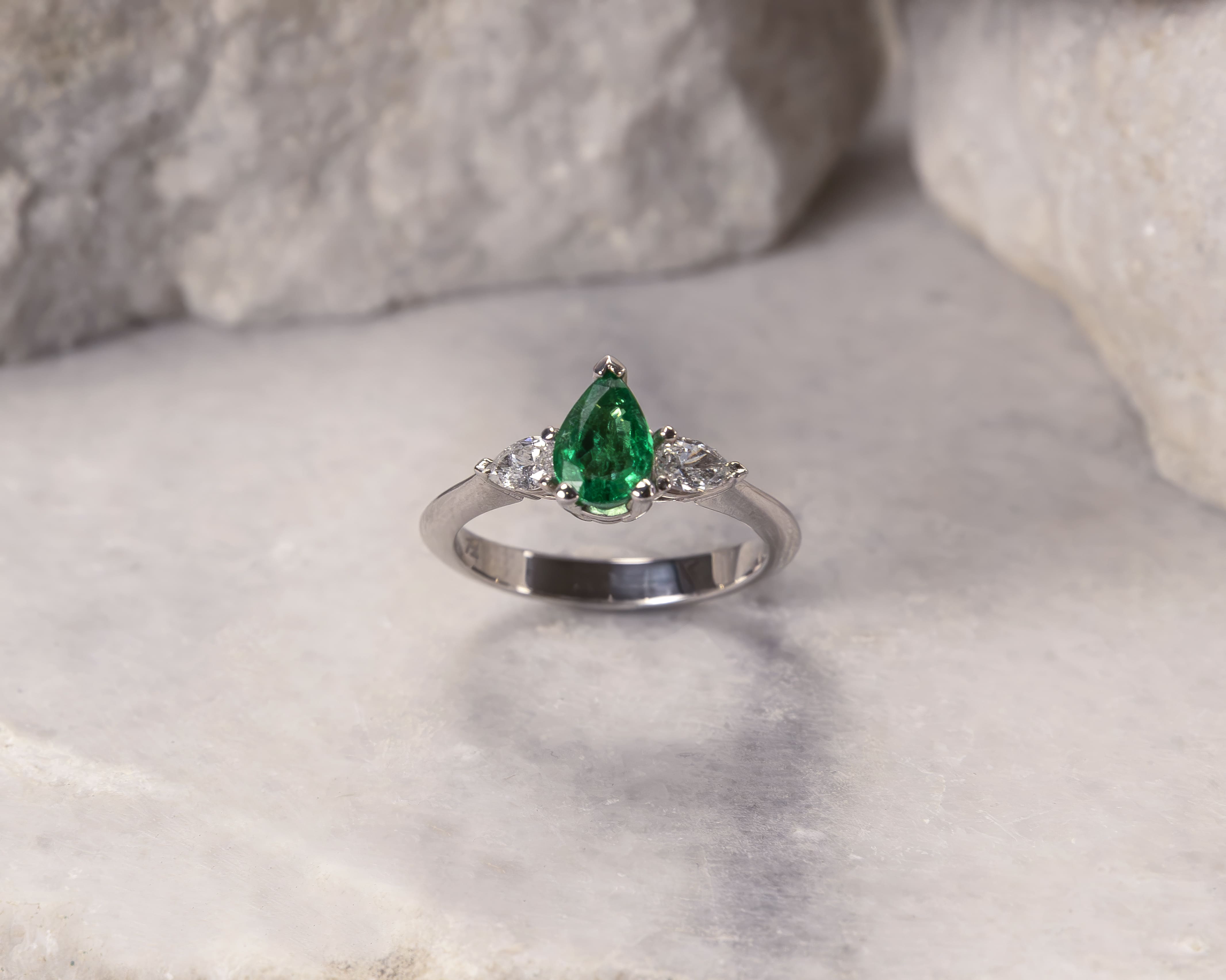 Silver ring featuring a pear-shaped green emerald flanked by two pear-shaped diamonds.