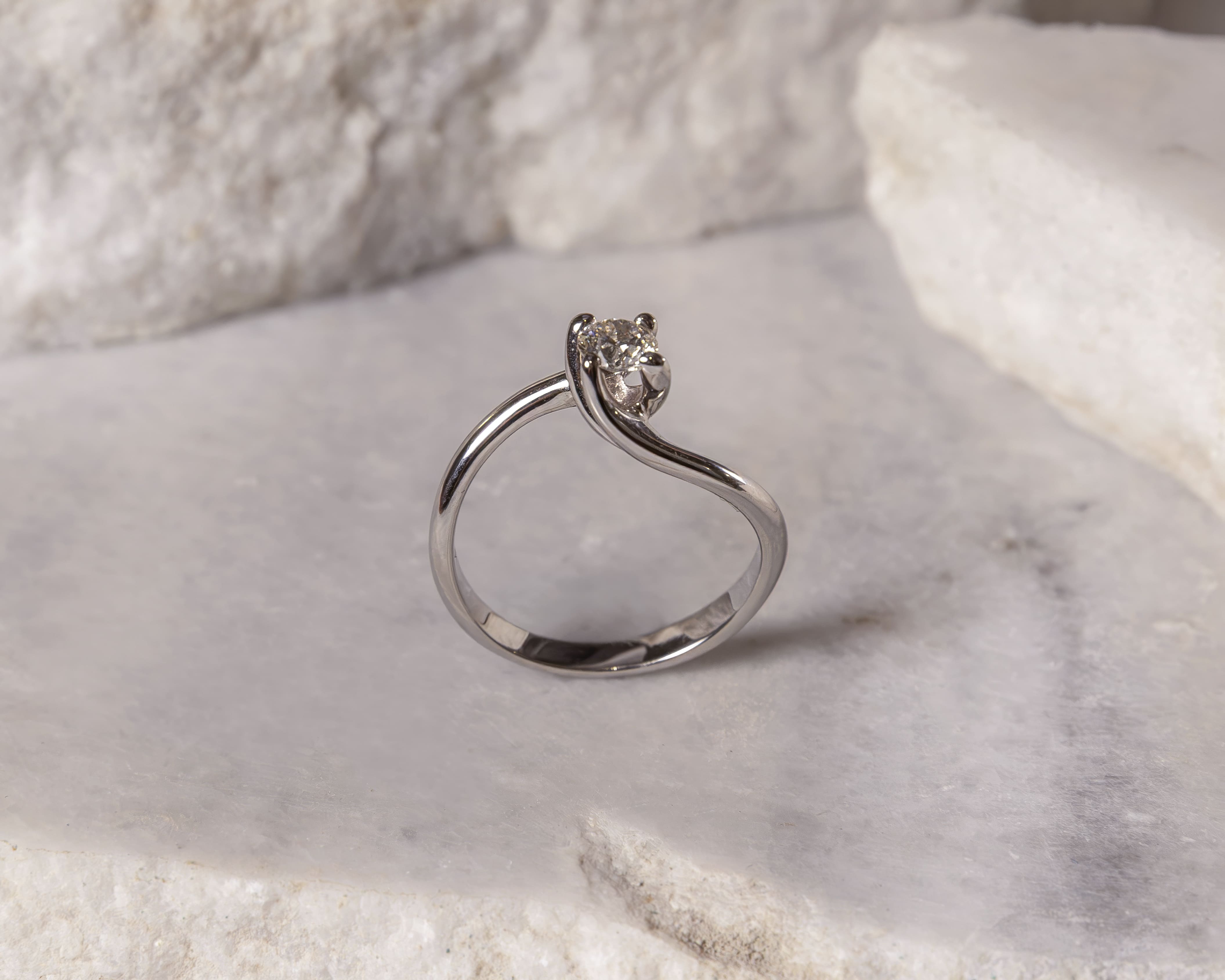 Elegant silver ring with a small diamond set in a twisted band on a pale marble surface.