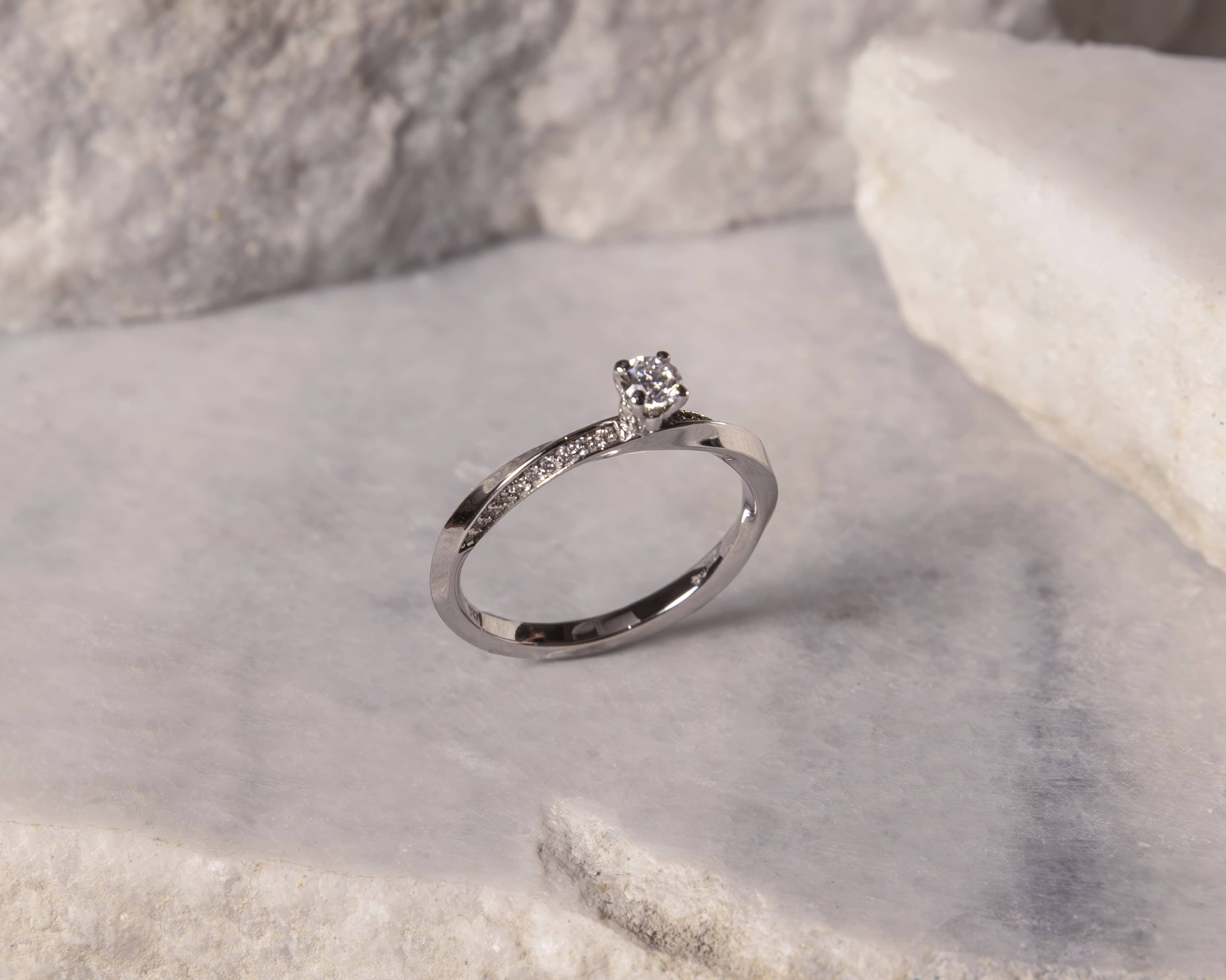 Silver ring with a solitaire diamond and small accent diamonds on a marble surface.