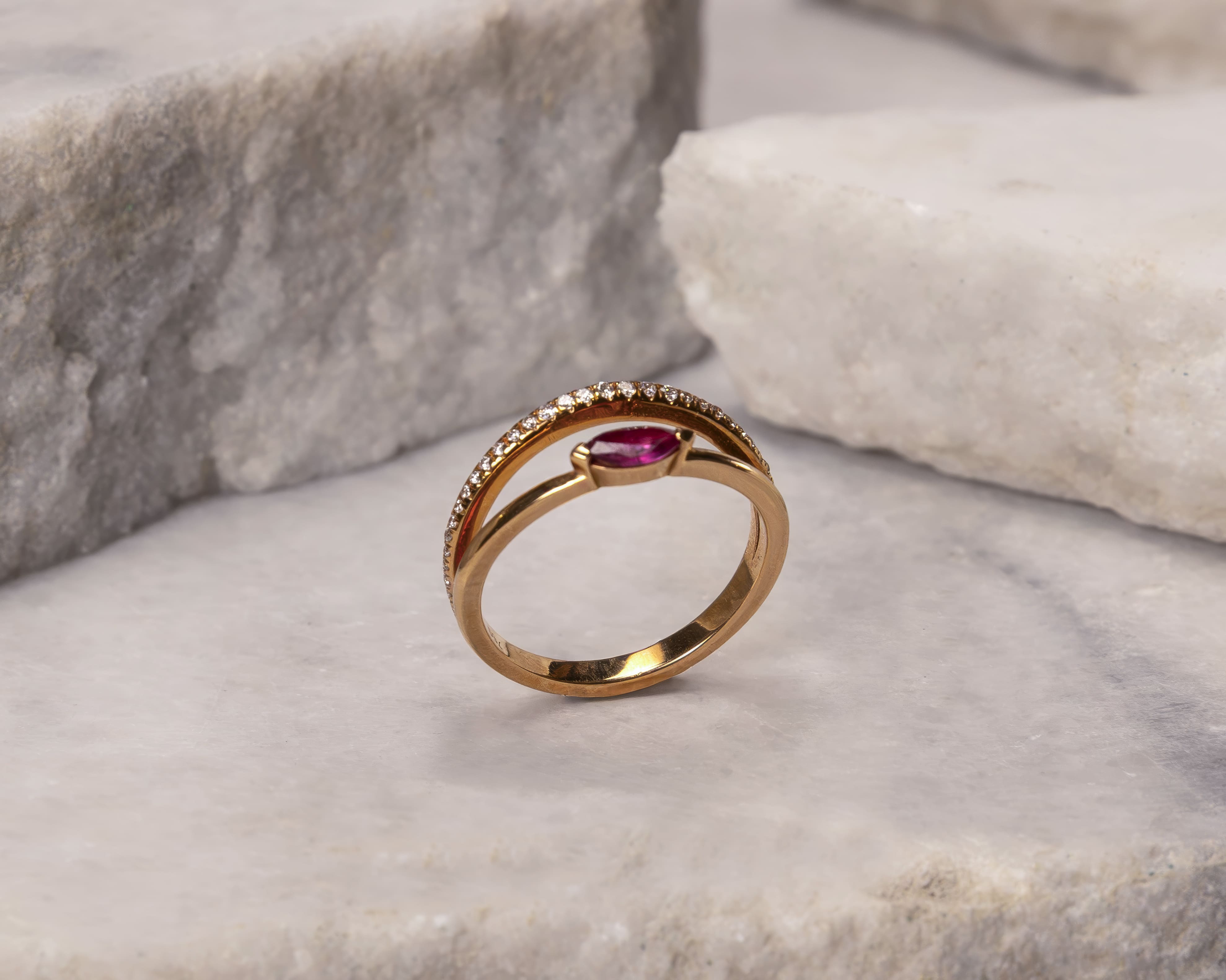 Gold ring with a central marquise-cut red gemstone and a curved row of small diamonds on a marble surface.
