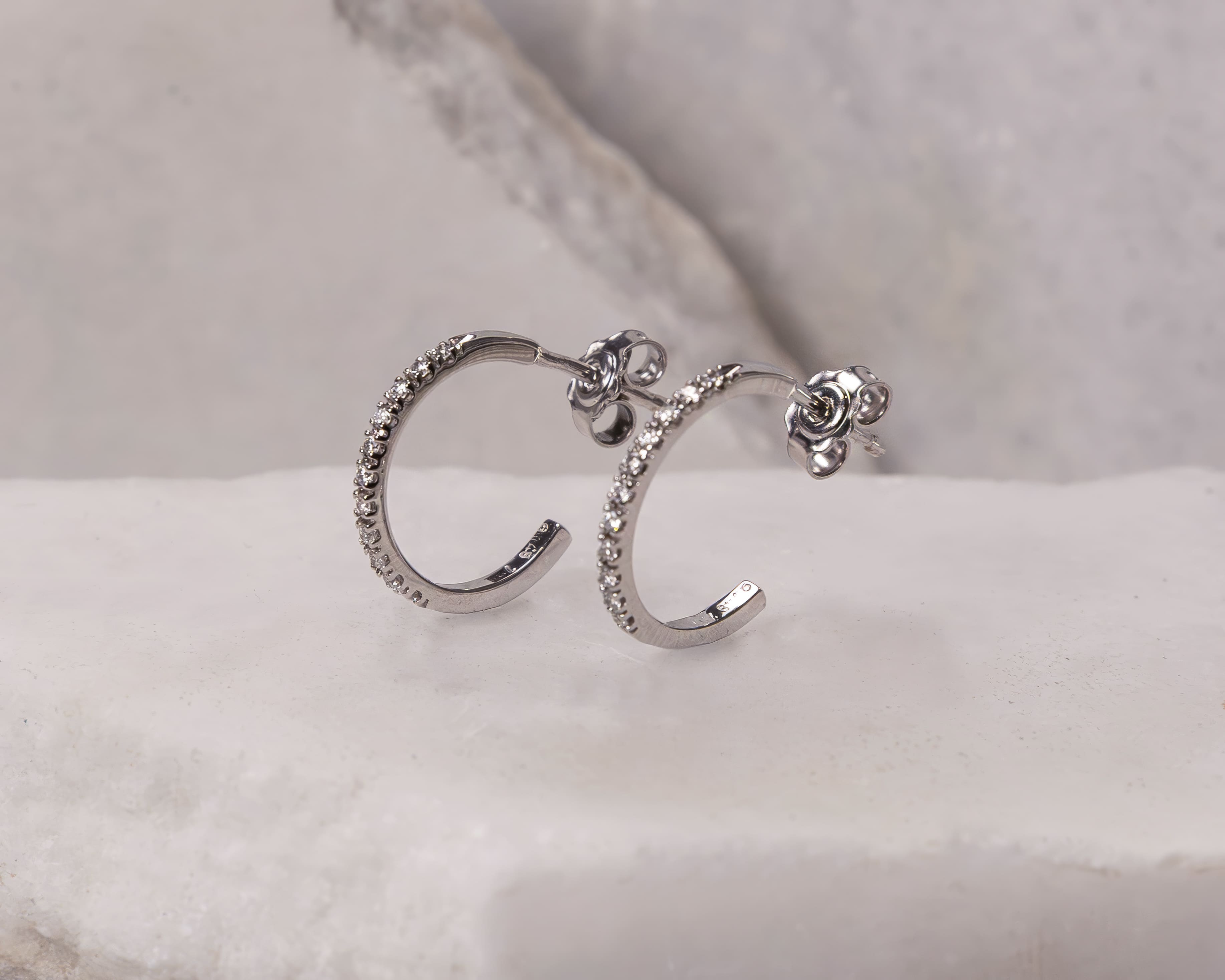 Pair of silver hoop earrings encrusted with small clear gemstones on white marble surface.