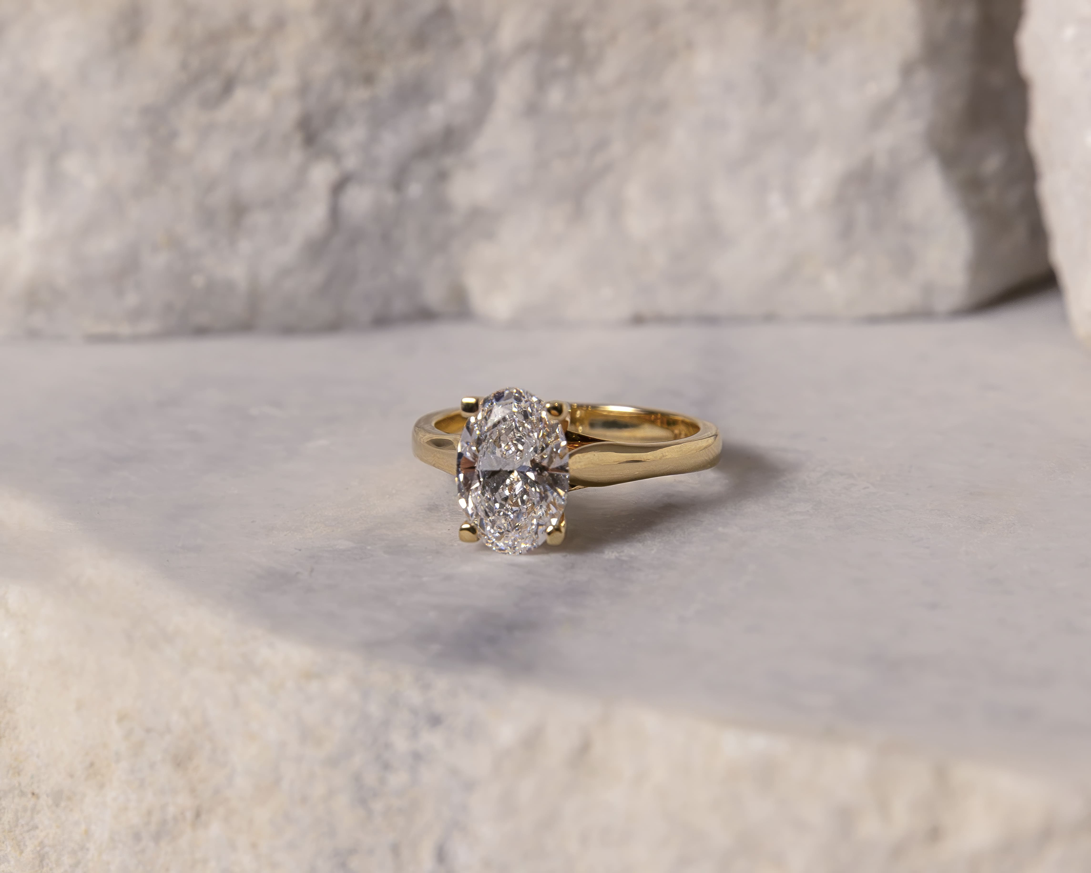Gold ring with an oval-cut diamond set on a light stone surface with a blurred stone background.