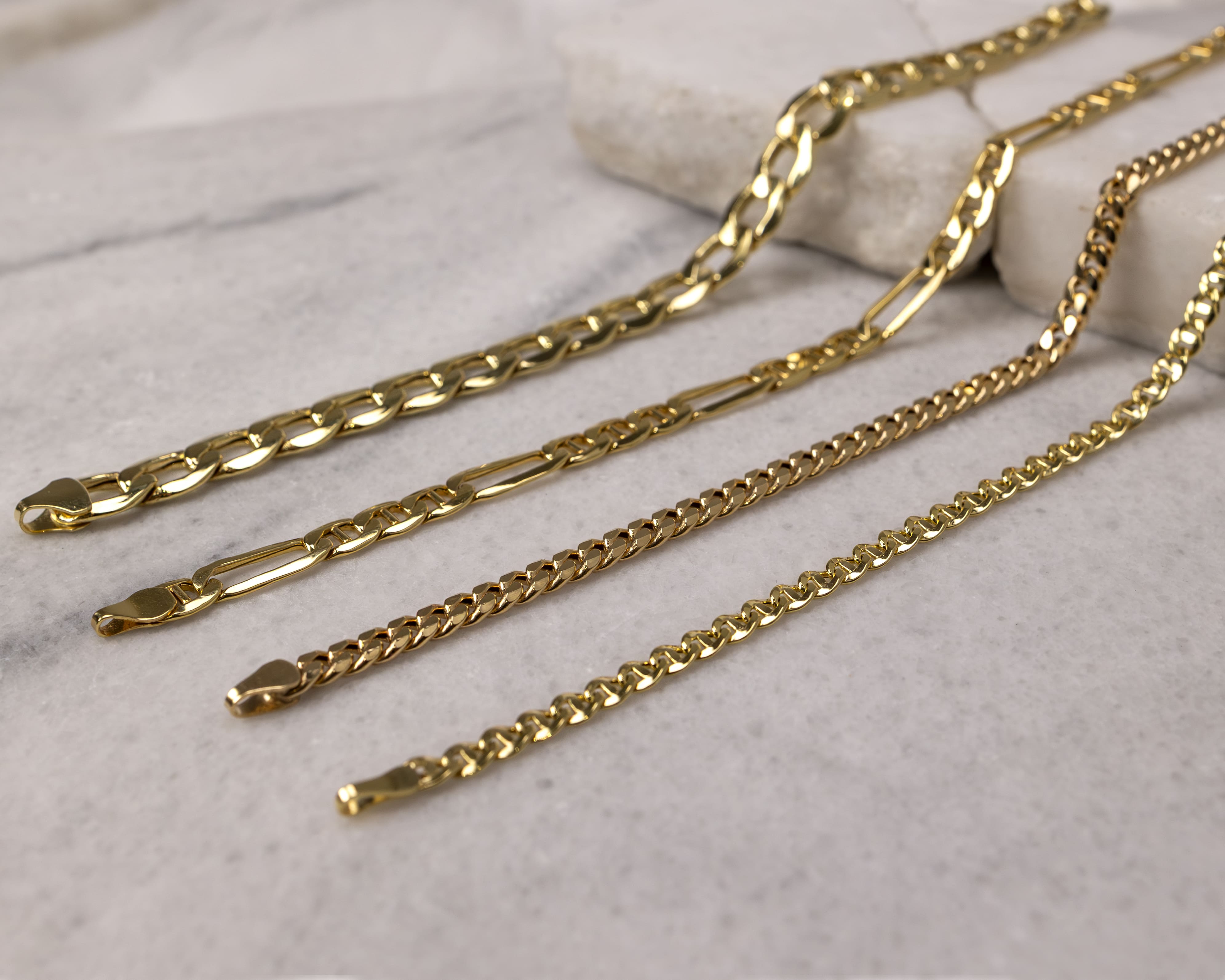 Four different styles of gold chains laid out on a marble surface.