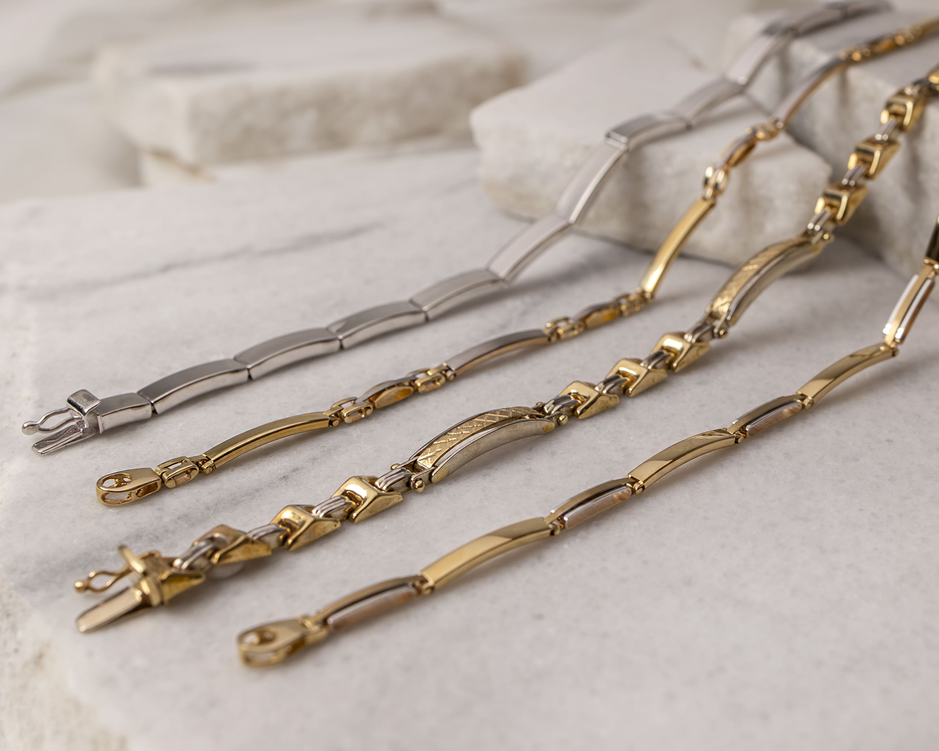 Close-up of four elegant metal bracelets in gold and silver tones displayed on a marble surface.