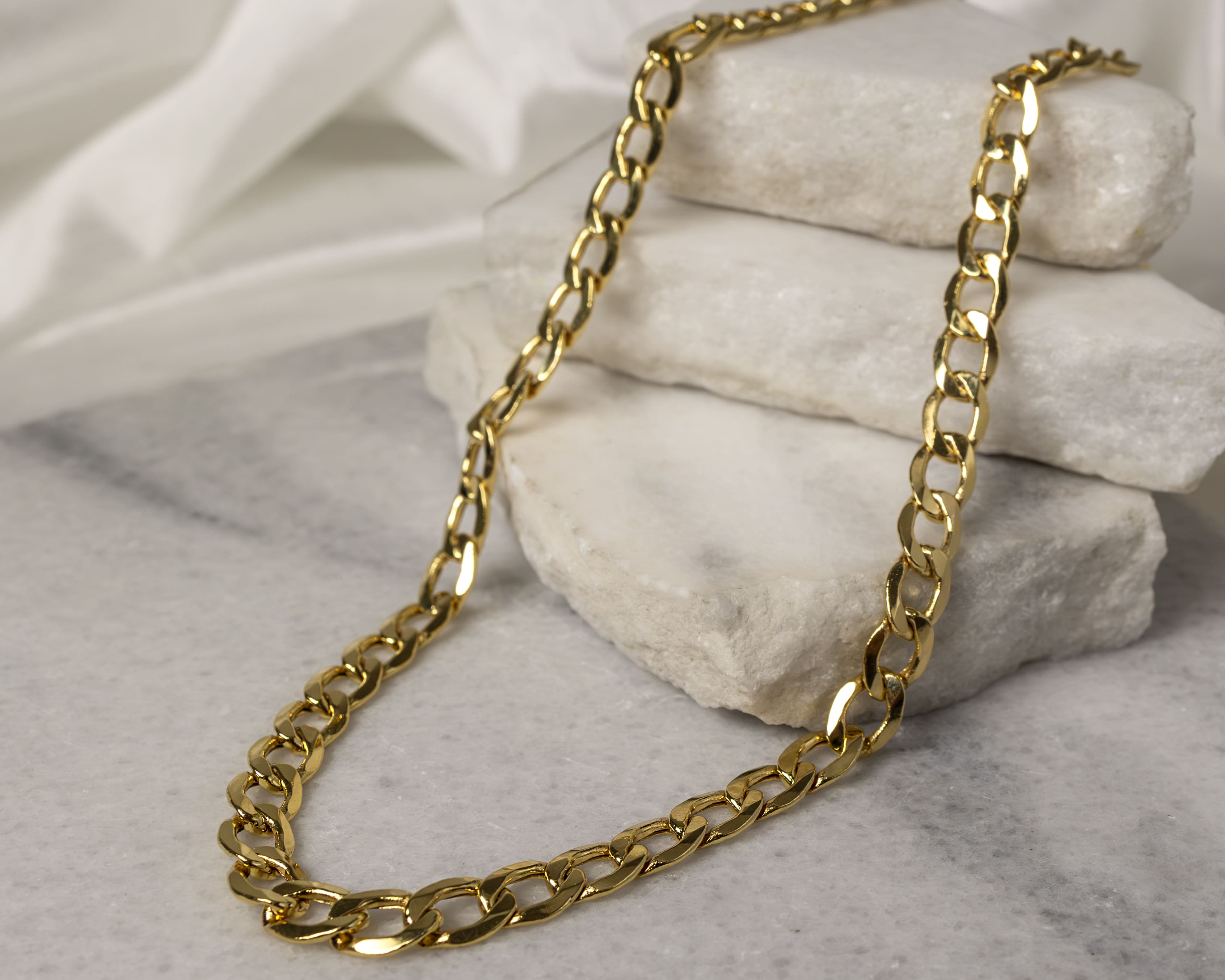 Gold chain necklace draped over stacked white stone slabs on a marble surface.