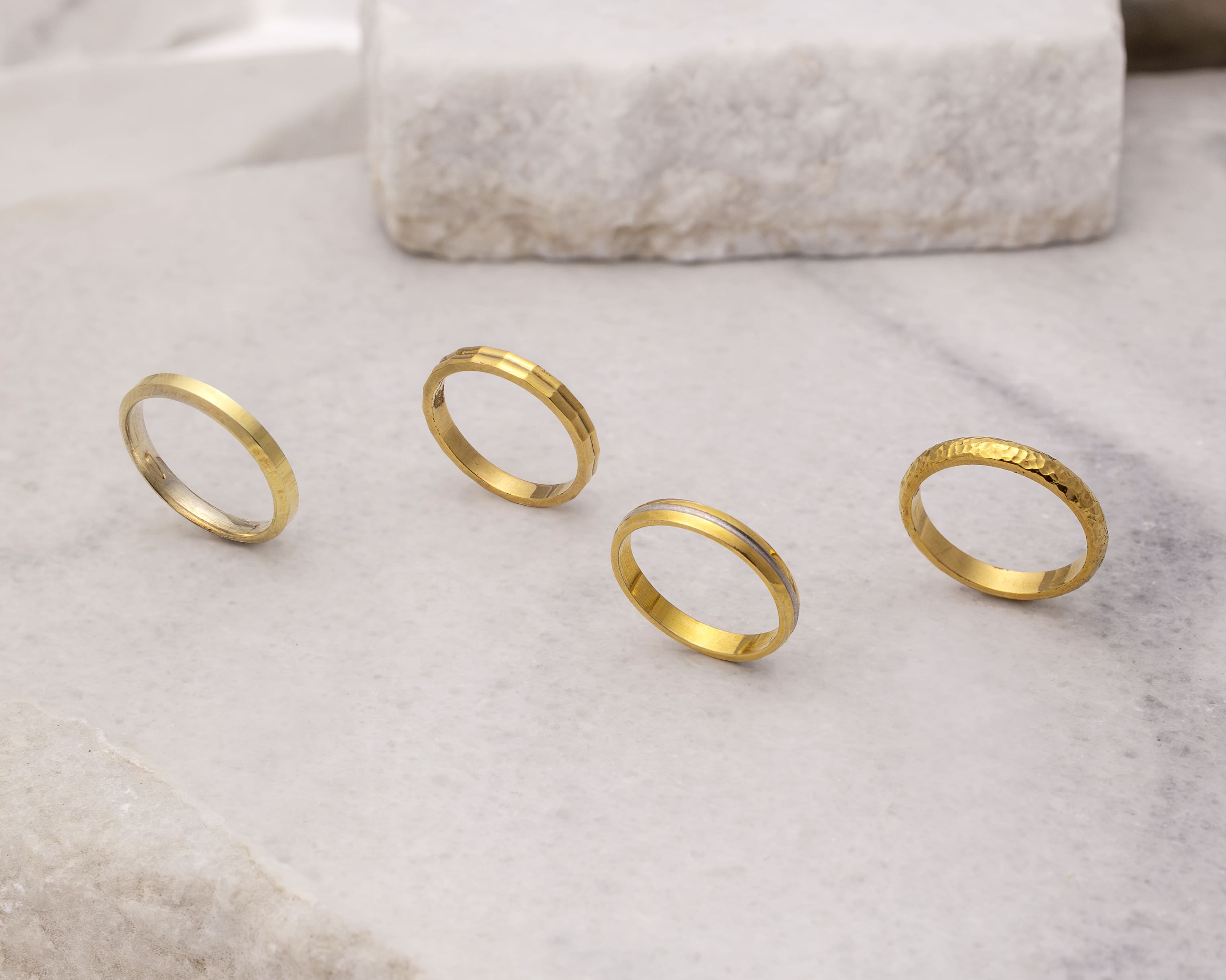 Four gold rings with varying textures displayed on a light stone surface.