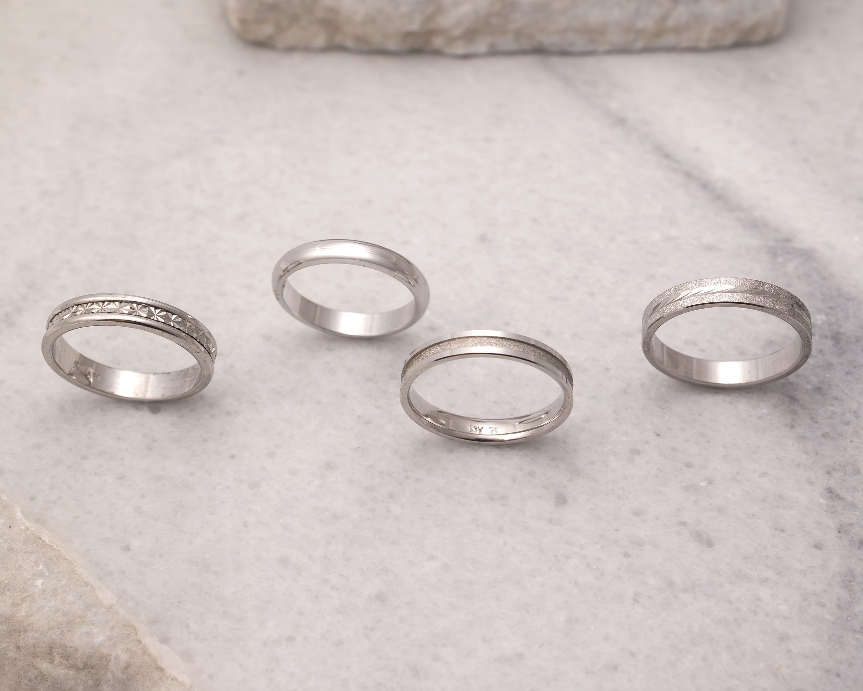 Four silver rings placed on a light marble surface, each with distinct patterns and designs.