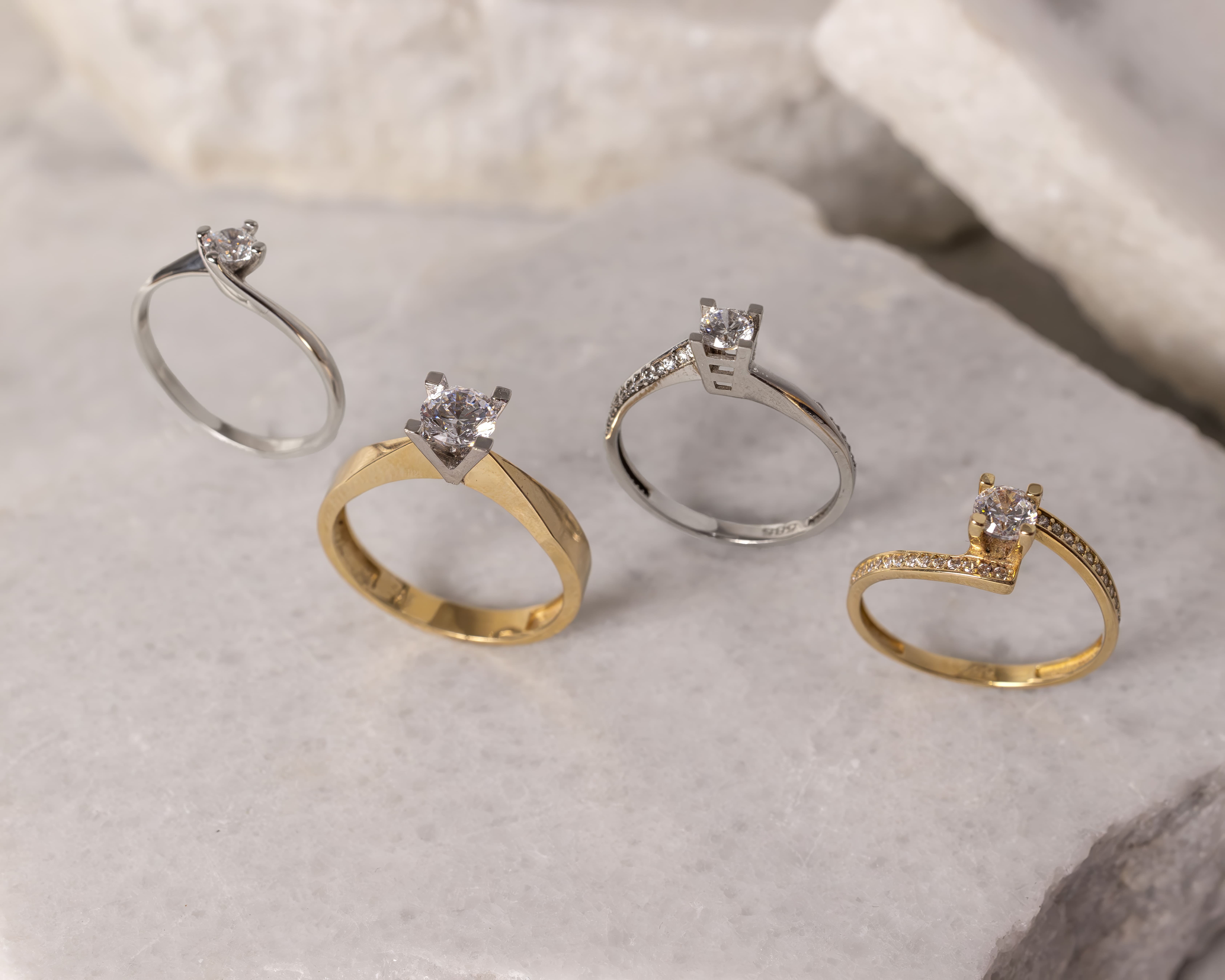Four diamond engagement rings in gold and silver on a light marble surface.