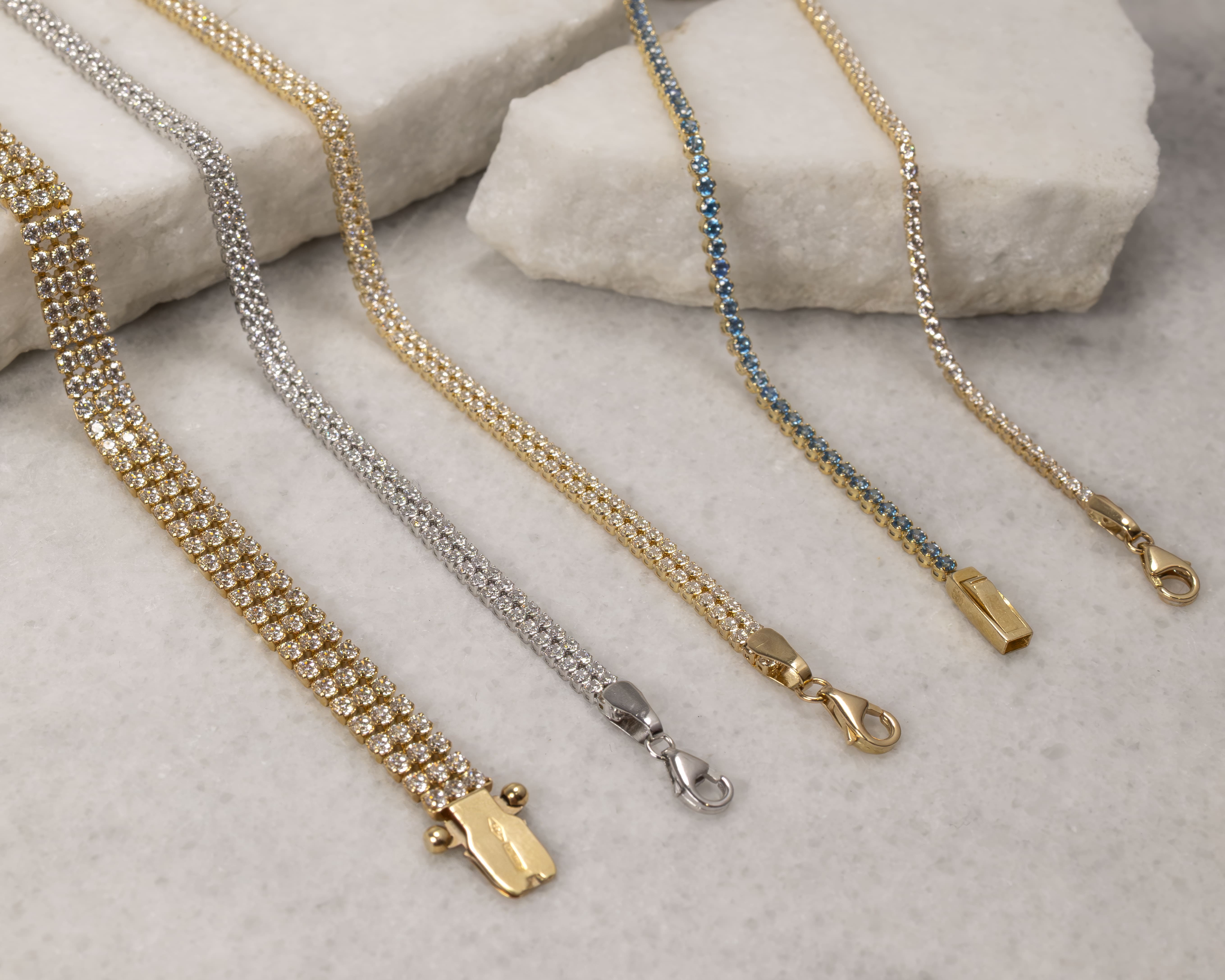 Five sparkling bracelets with gold and silver clasps displayed on a light marble surface.