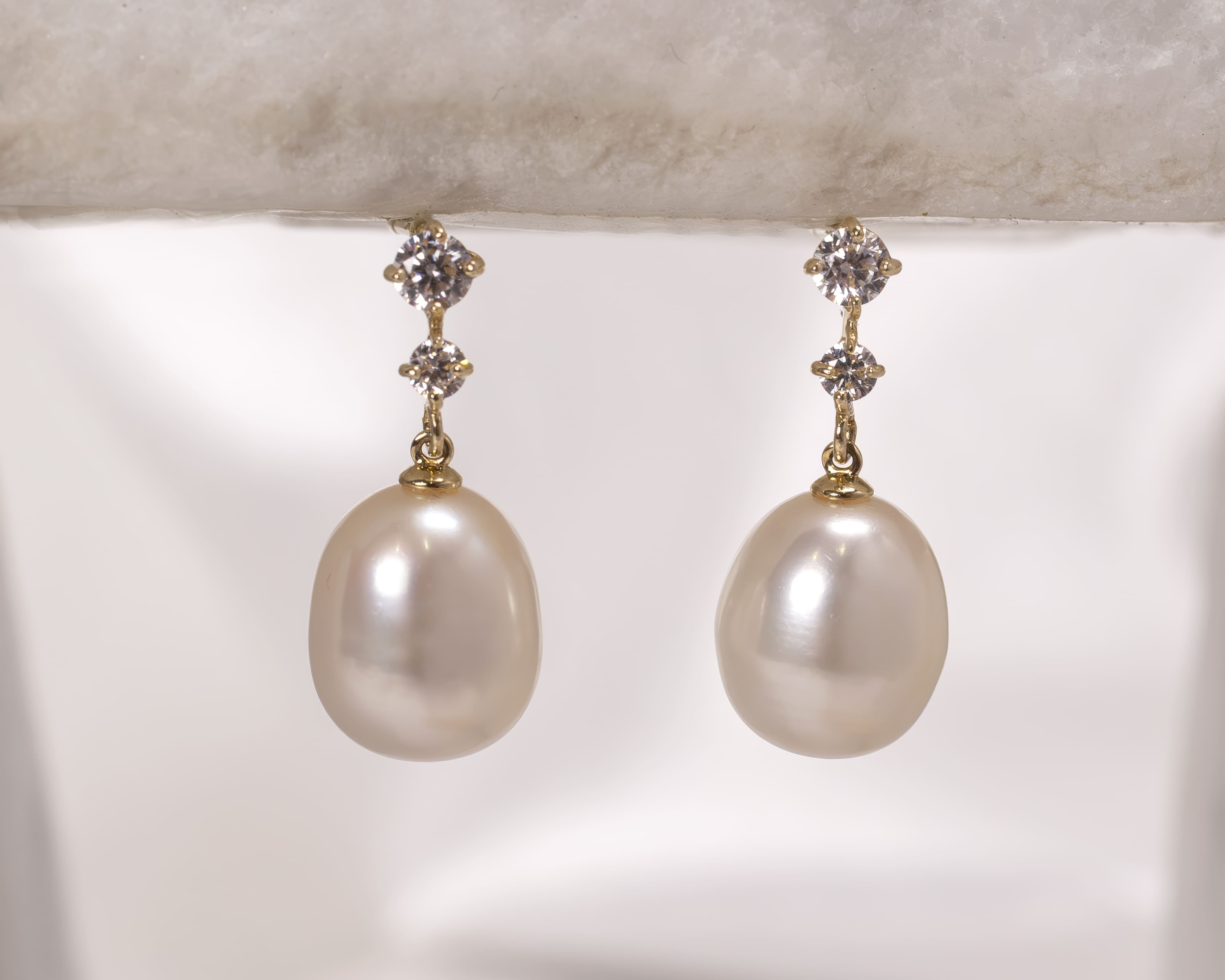 Pair of elegant gold earrings each featuring a large white pearl drop and two small round diamonds.