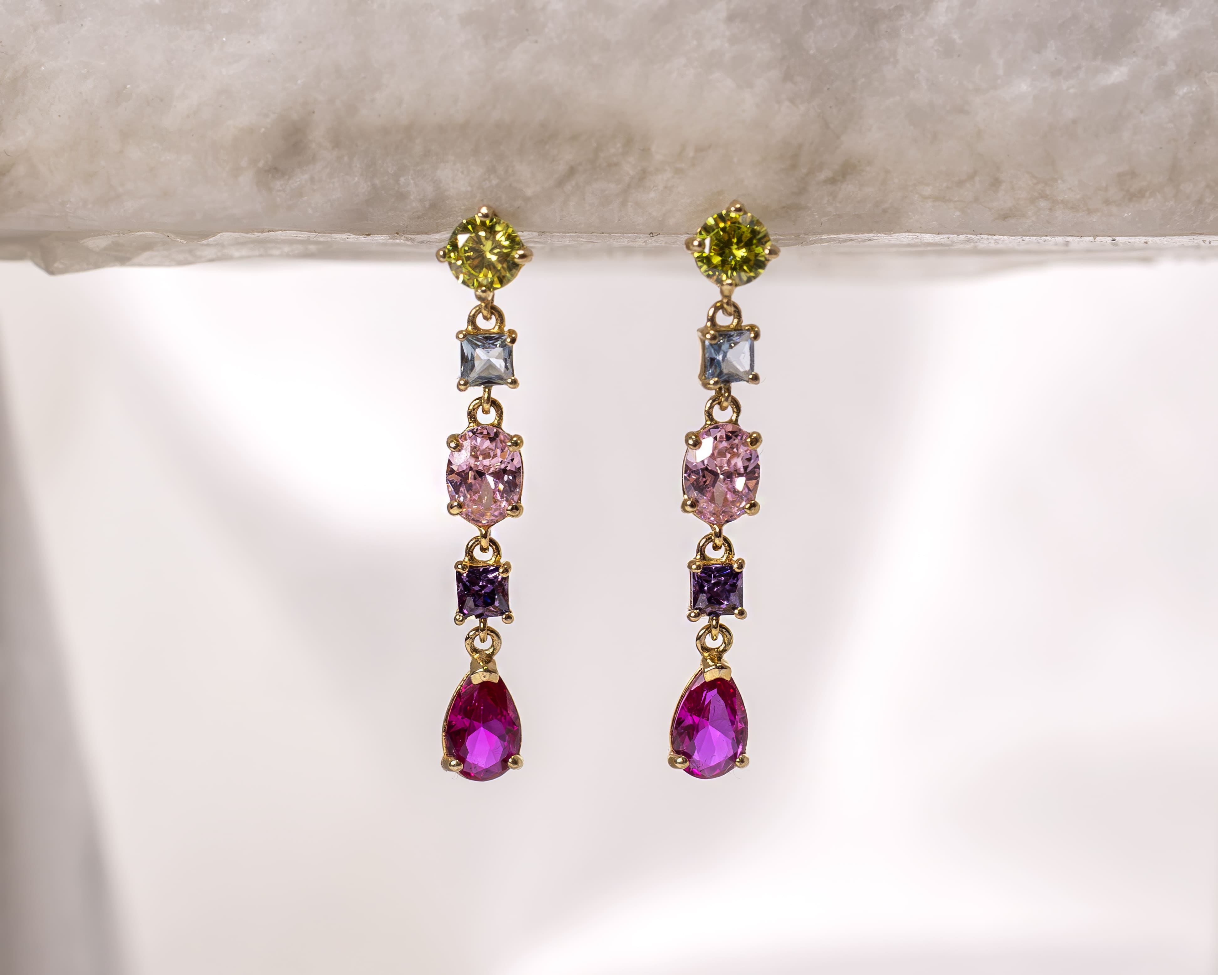 Pair of dangling gold earrings featuring five colorful gemstones each in green, light blue, pink, purple, and dark pink teardrop shapes.