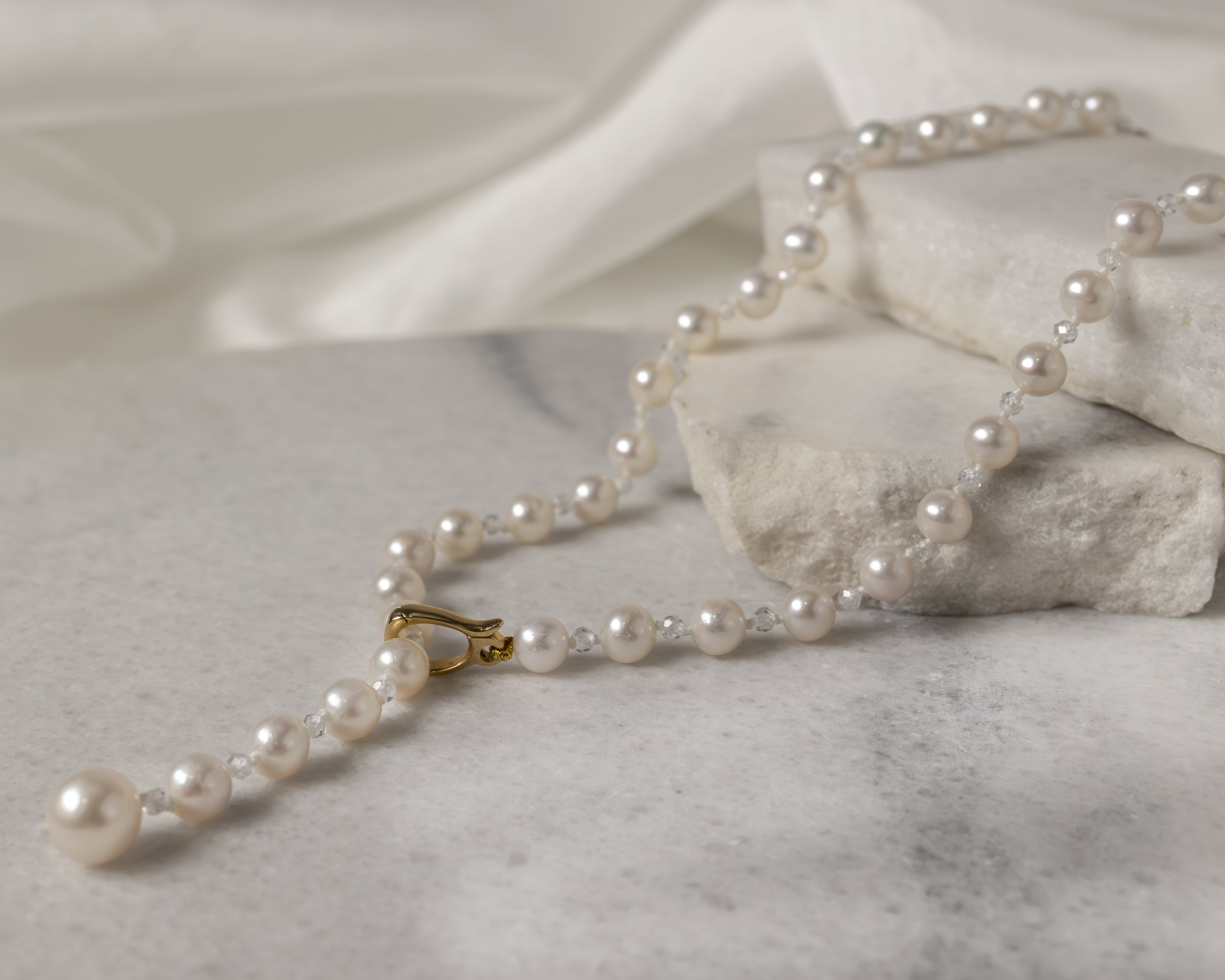 String of white pearls necklace with a gold clasp resting on white marble slabs.