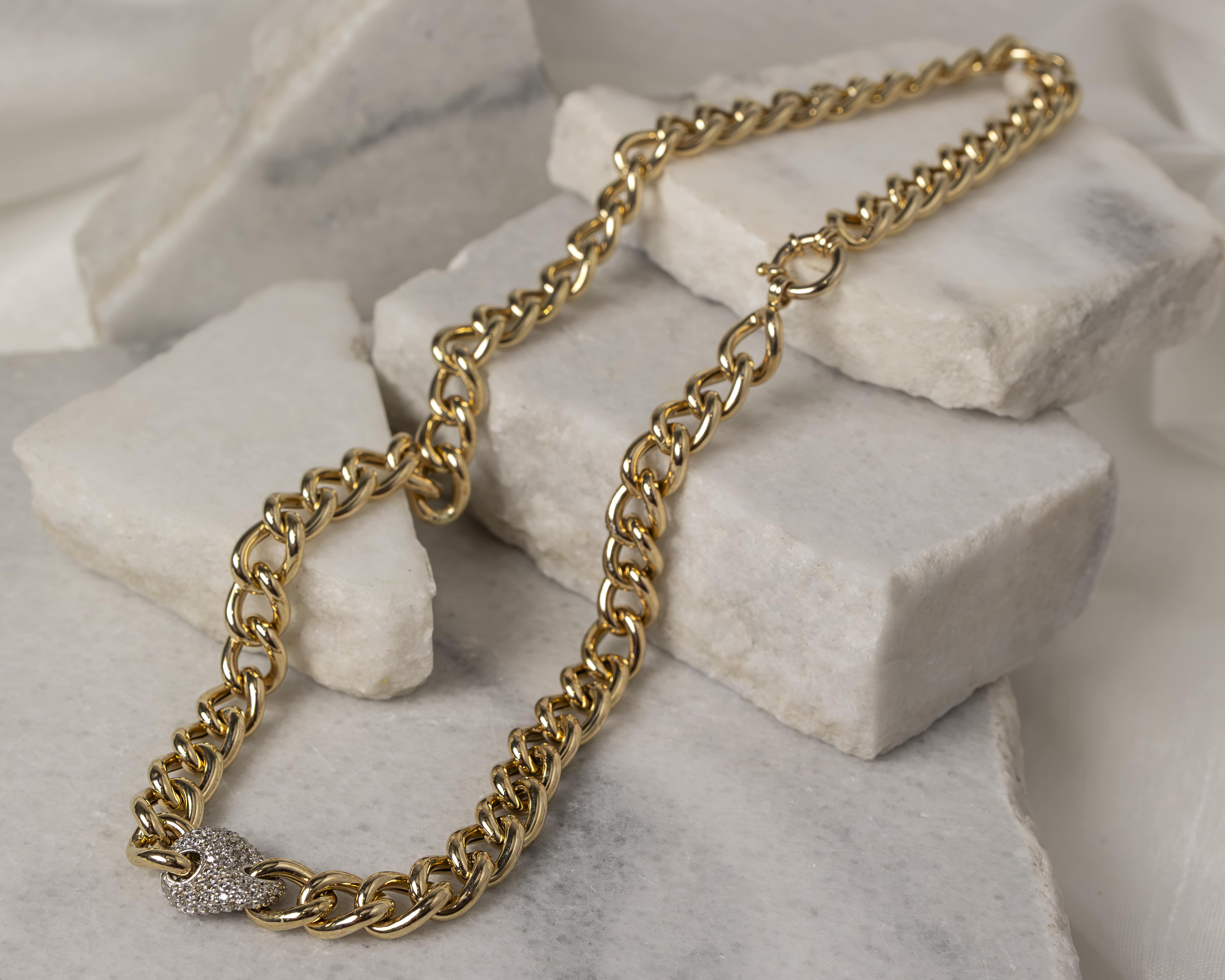 Gold chain necklace with an oval-shaped diamond-encrusted clasp placed on white marble stones.
