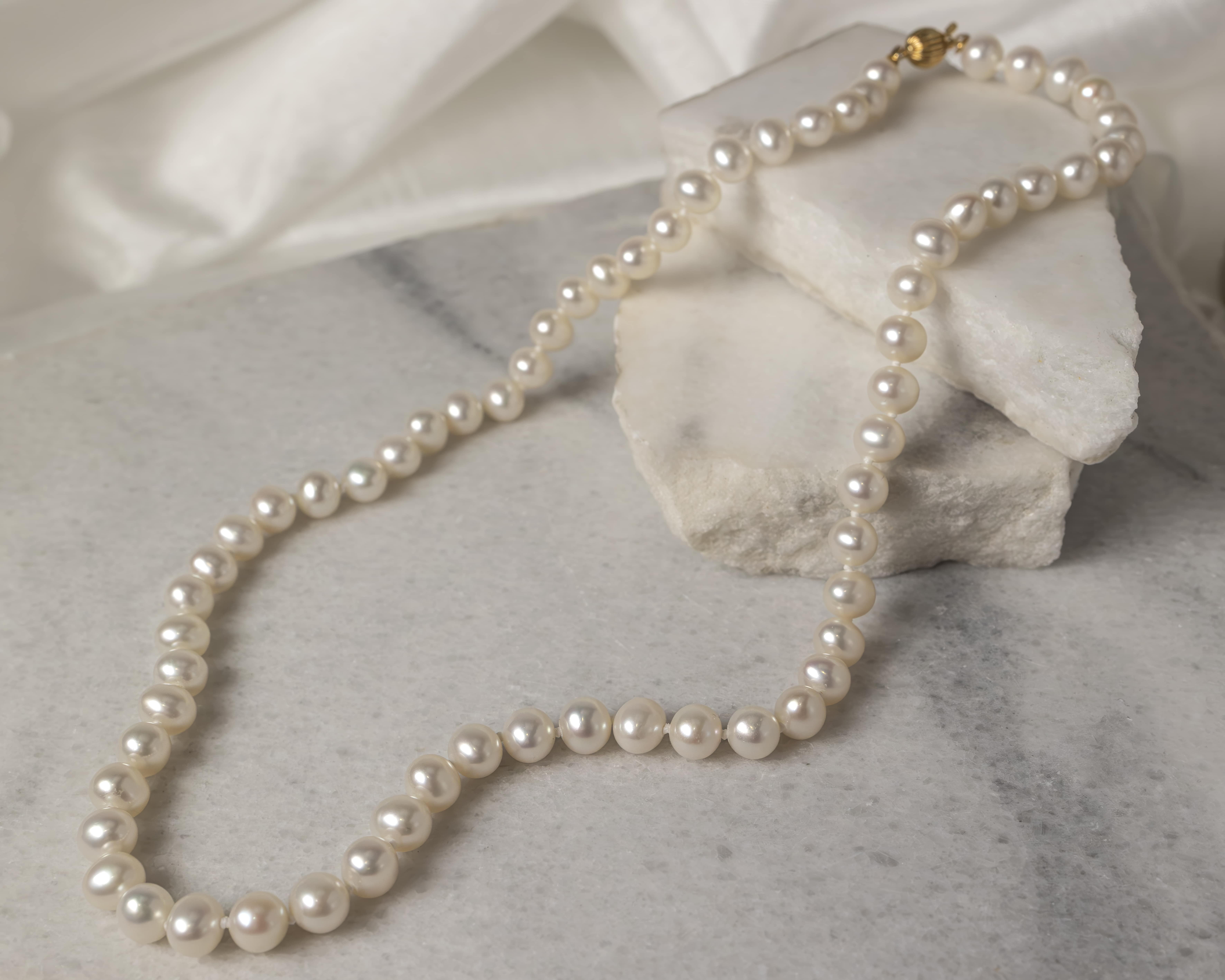 Single strand pearl necklace with a gold clasp displayed on white marble slabs.