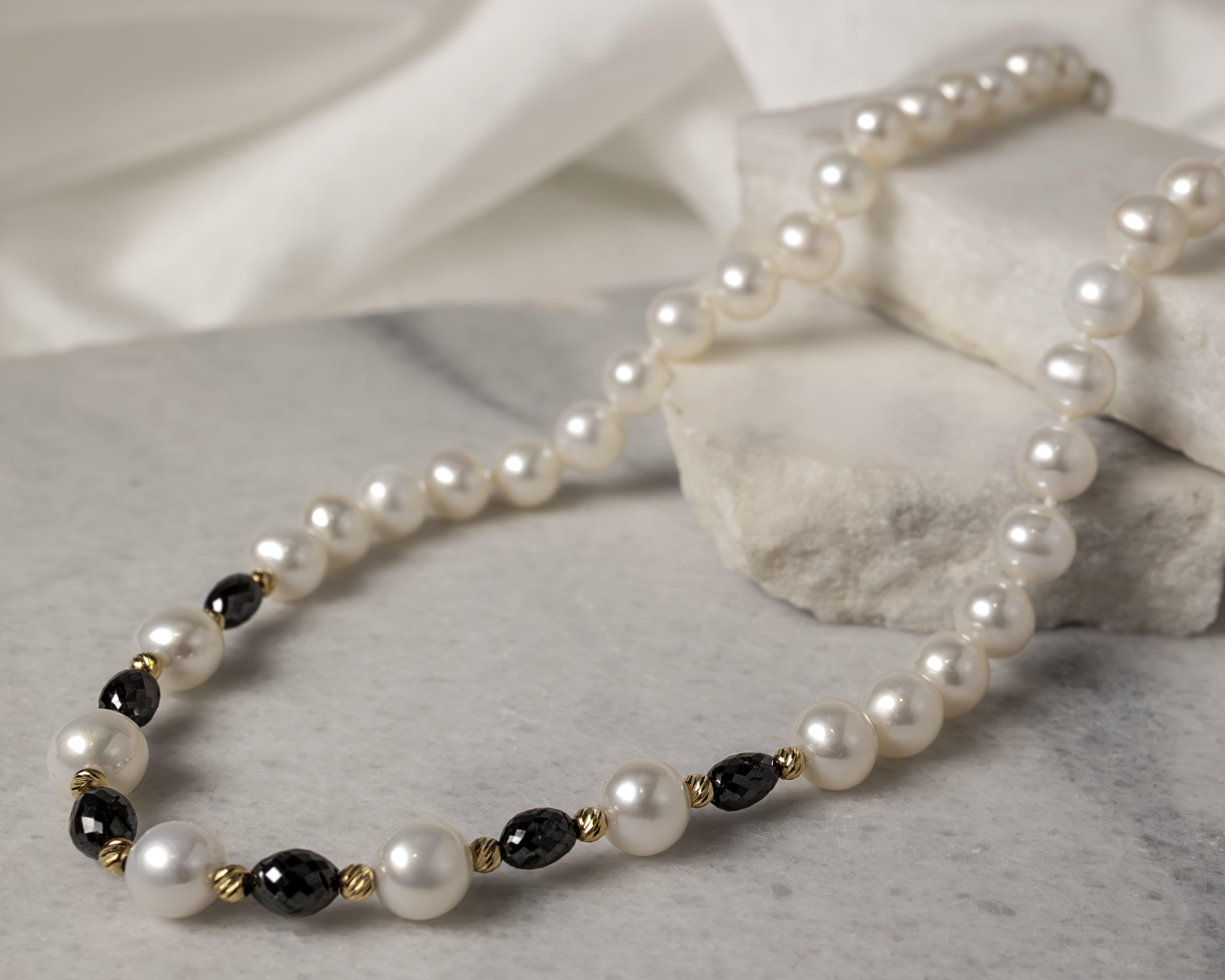 Elegant pearl necklace with alternating black and gold beads on a marble surface.