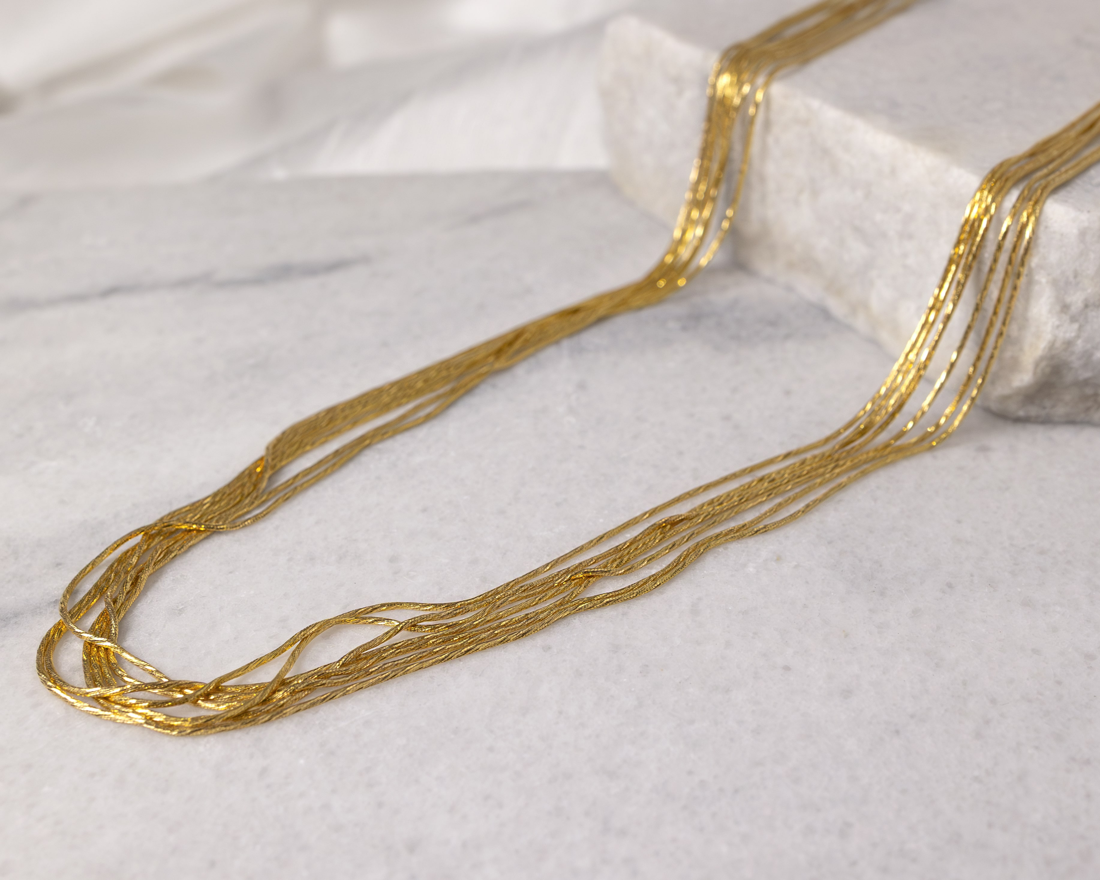 Close-up of a delicate multi-strand gold necklace displayed on a light-colored marble surface.