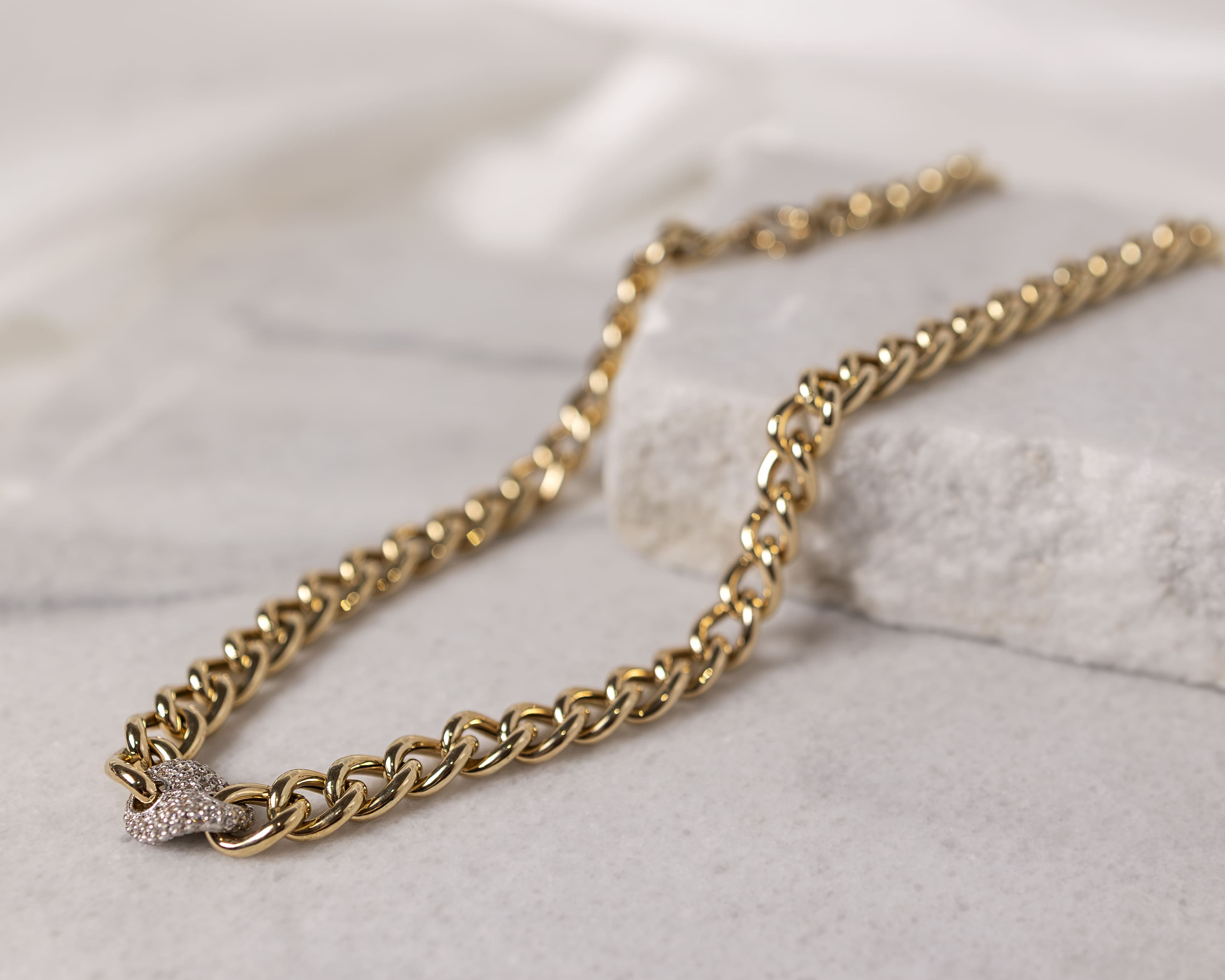 Close-up of a gold chain necklace with a silver clasp resting on a light stone surface.