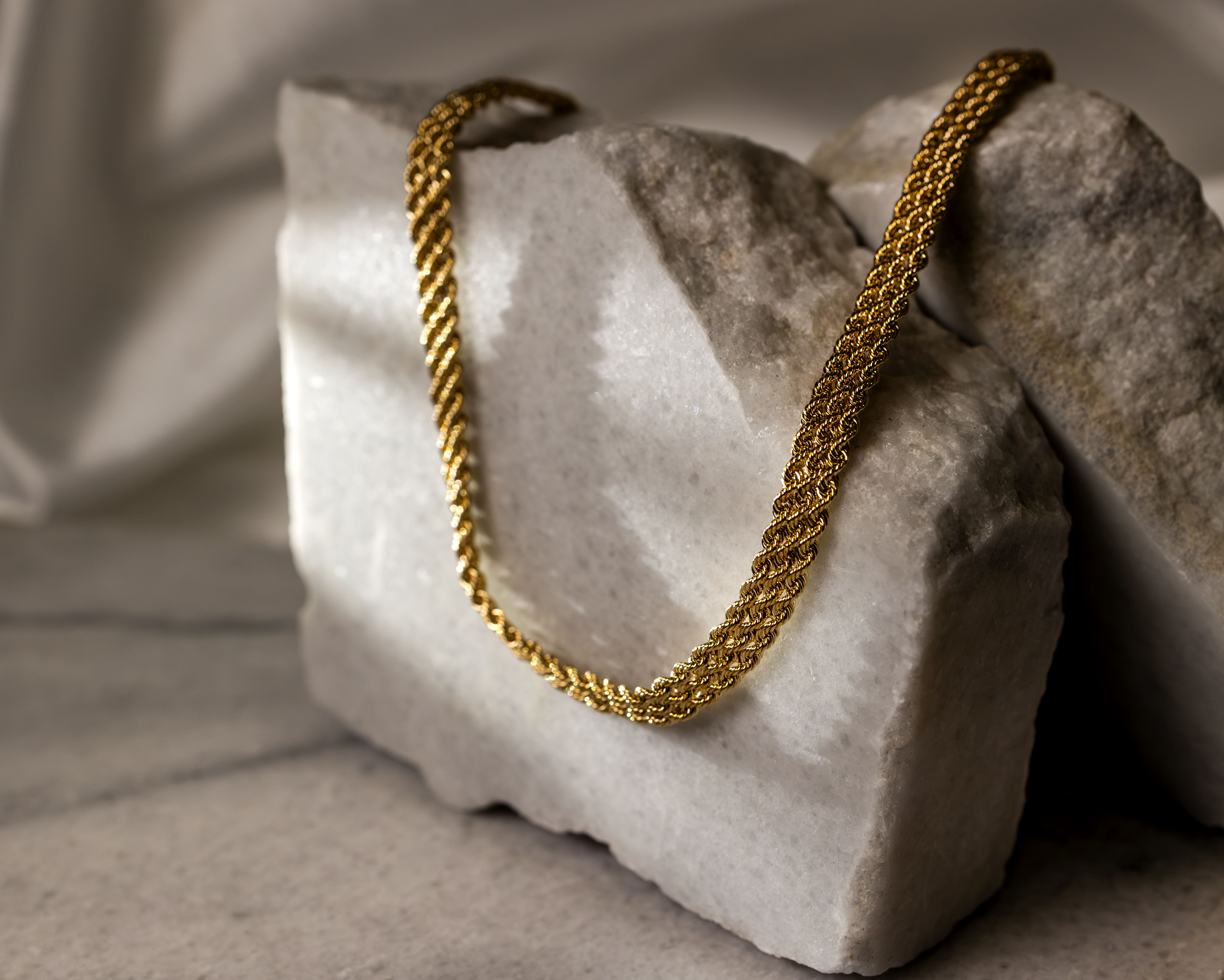 Gold rope chain necklace draped over textured white stone blocks on a gray surface.