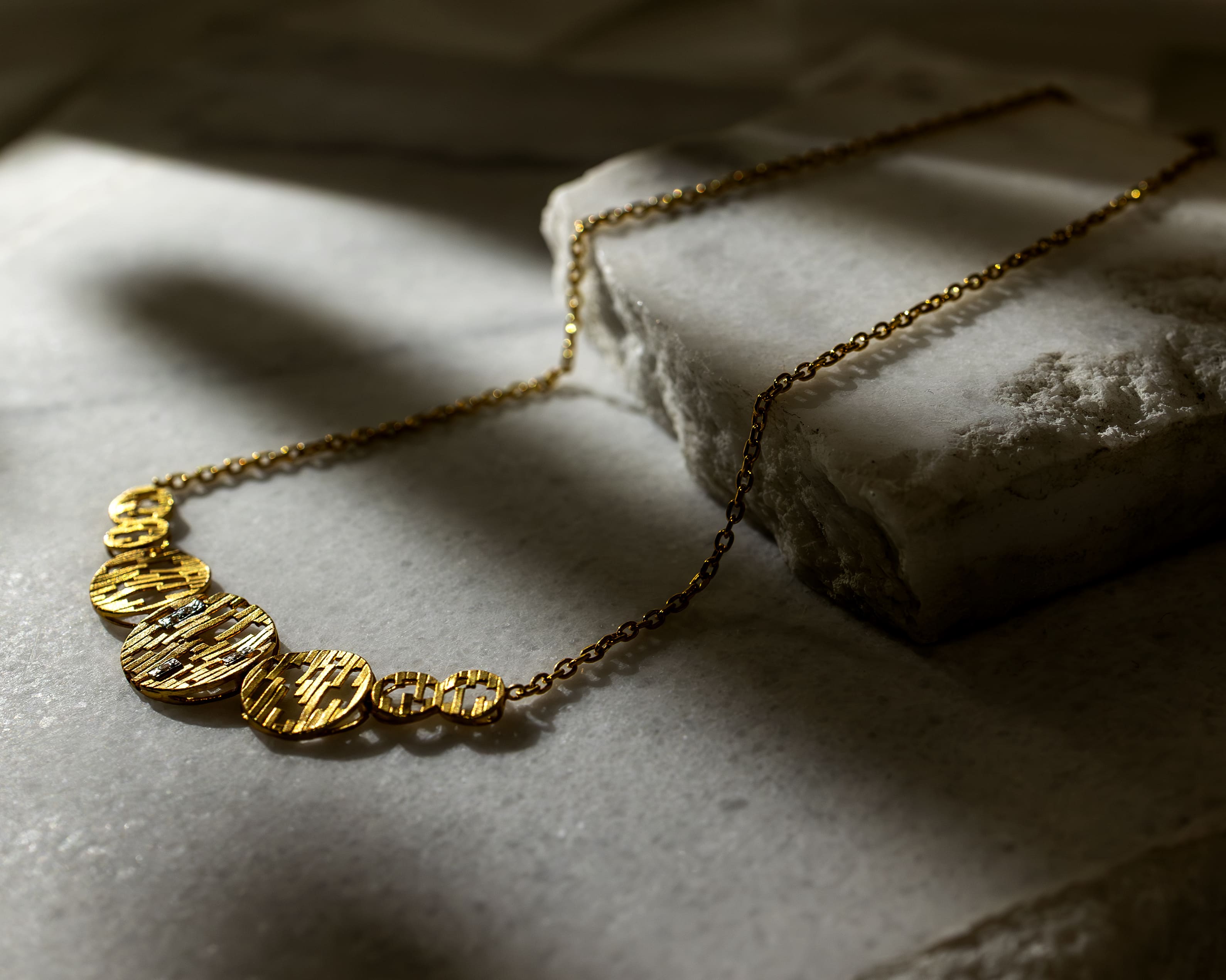 Gold necklace with textured circular pendants displayed on a marble surface.
