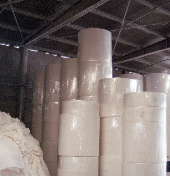 Bobine di carta bianca impilate in magazzino industriale con soffitto in metallo.