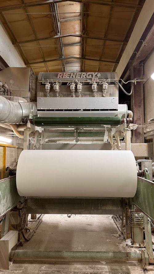 Macchinario industriale per la produzione di grandi rotoli di carta in un ambiente di fabbrica.