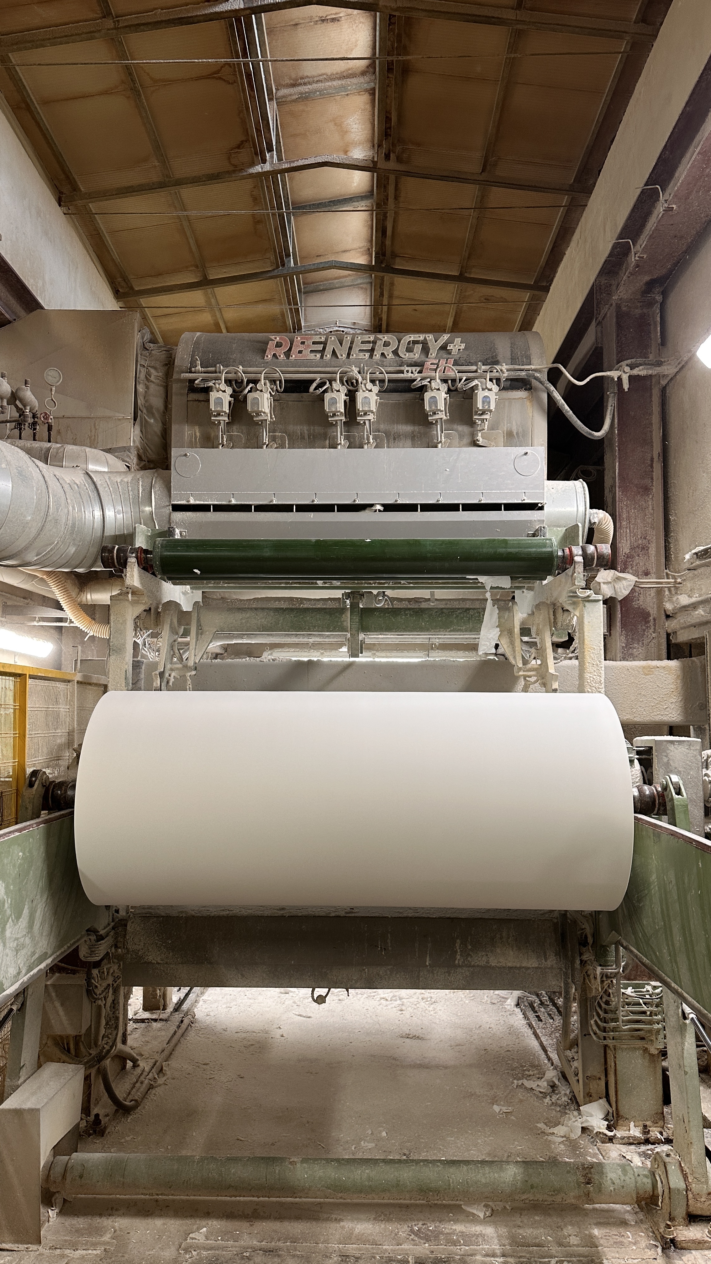 Macchinario industriale per la produzione di grandi rotoli di carta in un ambiente di fabbrica.