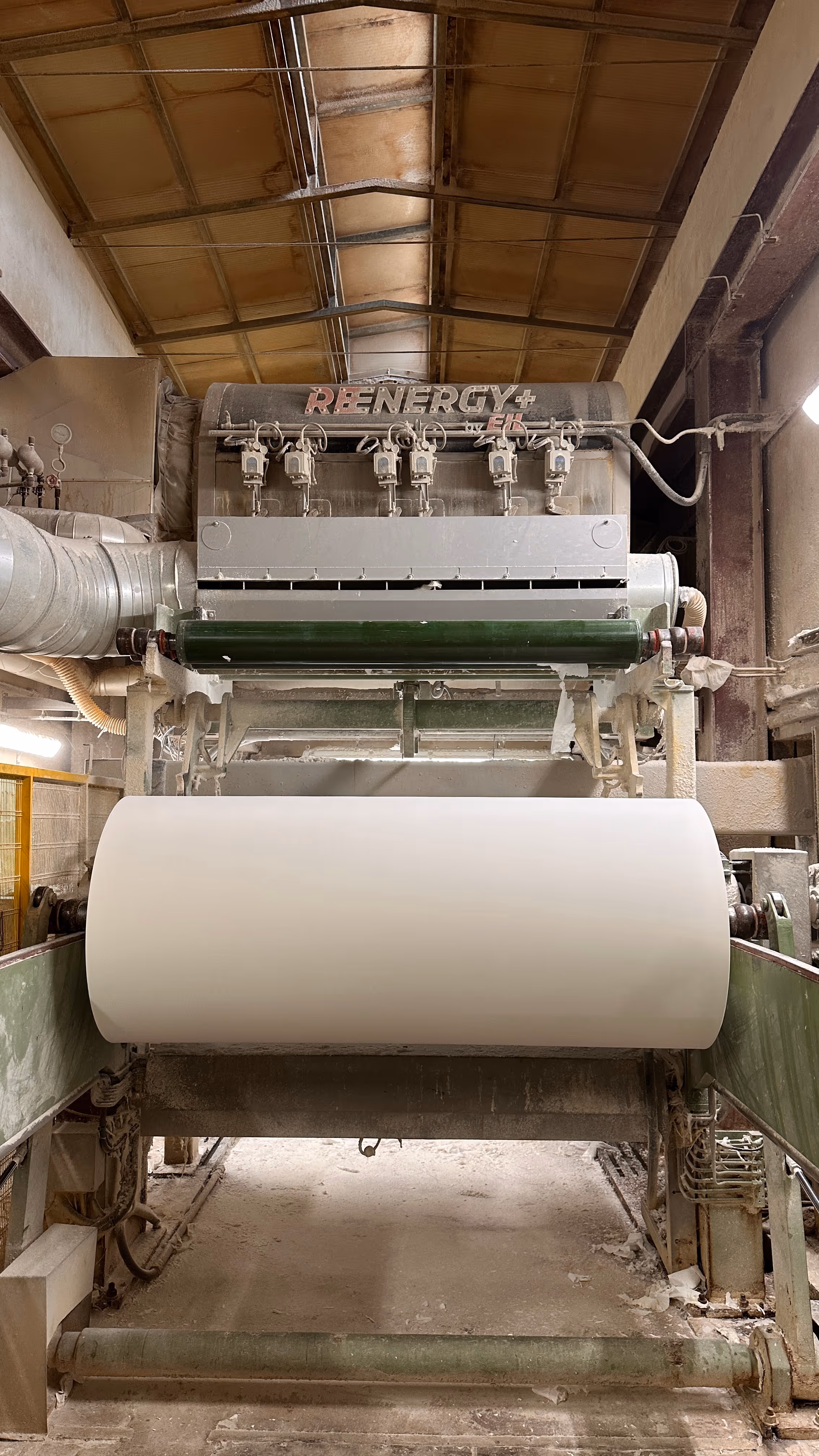 Macchinario industriale per la produzione di grandi rotoli di carta in un ambiente di fabbrica.