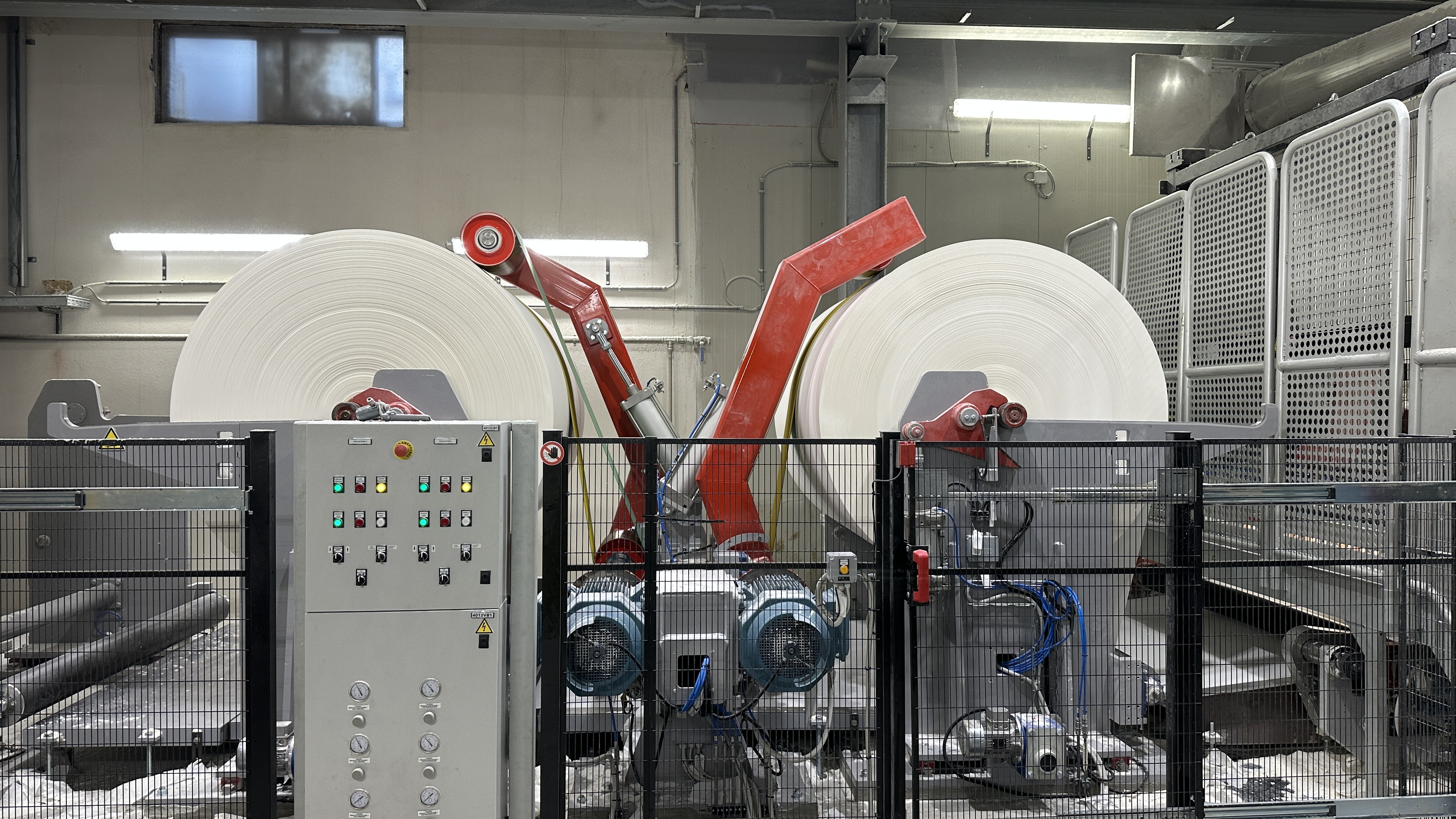 Macchinario industriale con due grandi rotoli di carta bianca installati in un impianto di produzione.