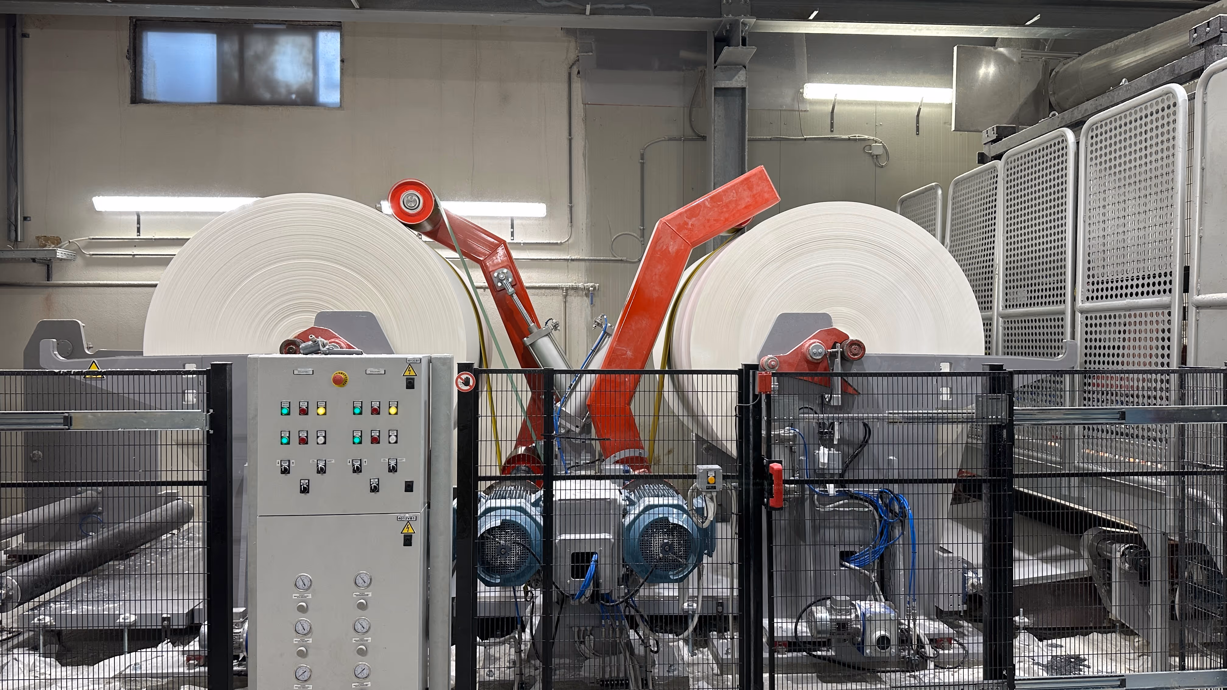 Macchinario industriale con due grandi rotoli di carta bianca installati in un impianto di produzione.