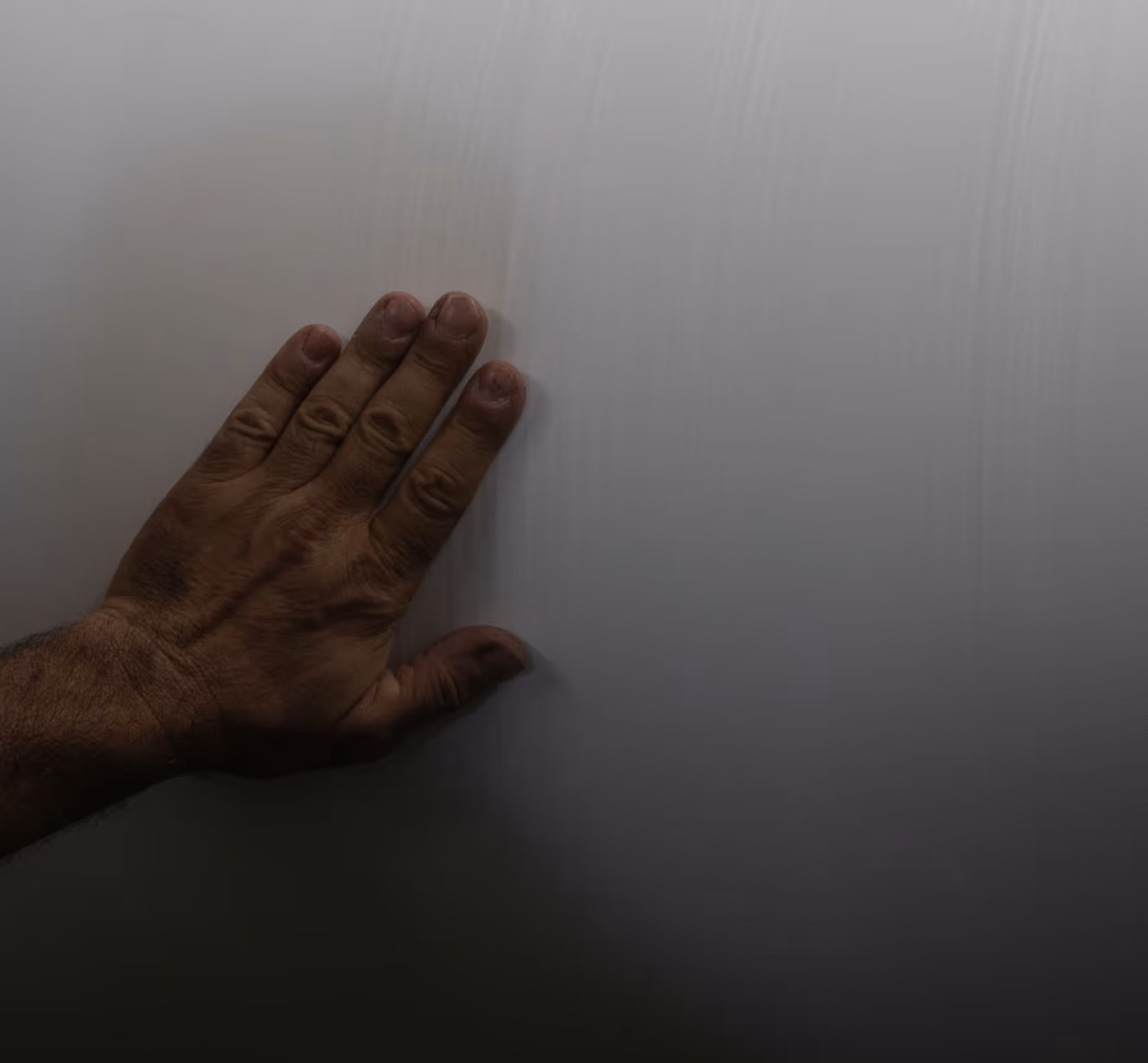 Mano maschile appoggiata su una superficie liscia e chiara, illuminata da una luce fioca.