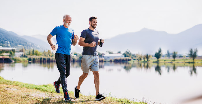 Retiree and their son jogging by a lake near the mountains