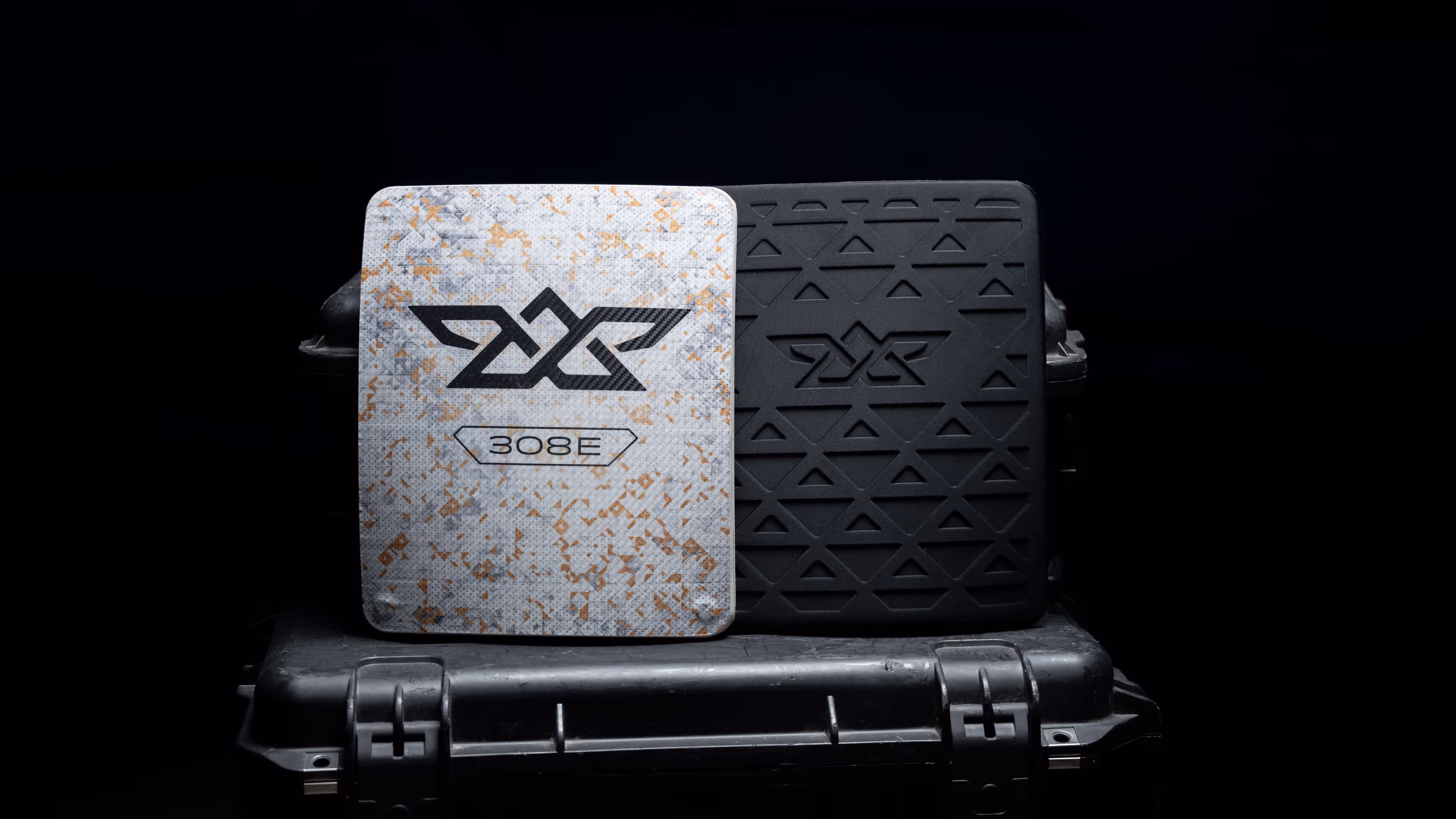 Two ballistic plates, one camouflaged with PX 308E logo and one black with embossed pattern, on a case.
