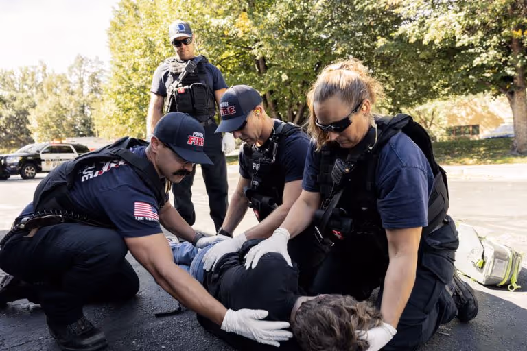 Firefighters restraining a person lying face down on a street during a daytime emergency.