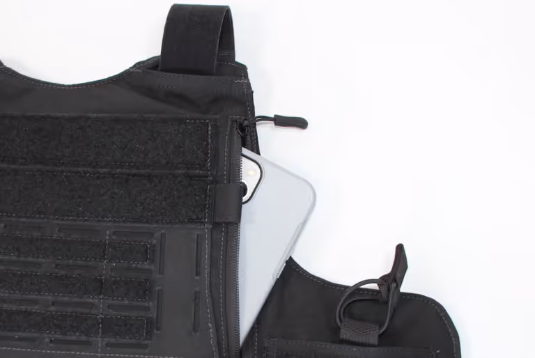Close-up of a black tactical vest pocket with a silver smartphone partially inside it.