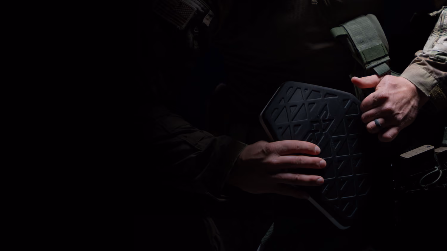 Person in tactical gear holding a black protective armor plate with geometric patterns.