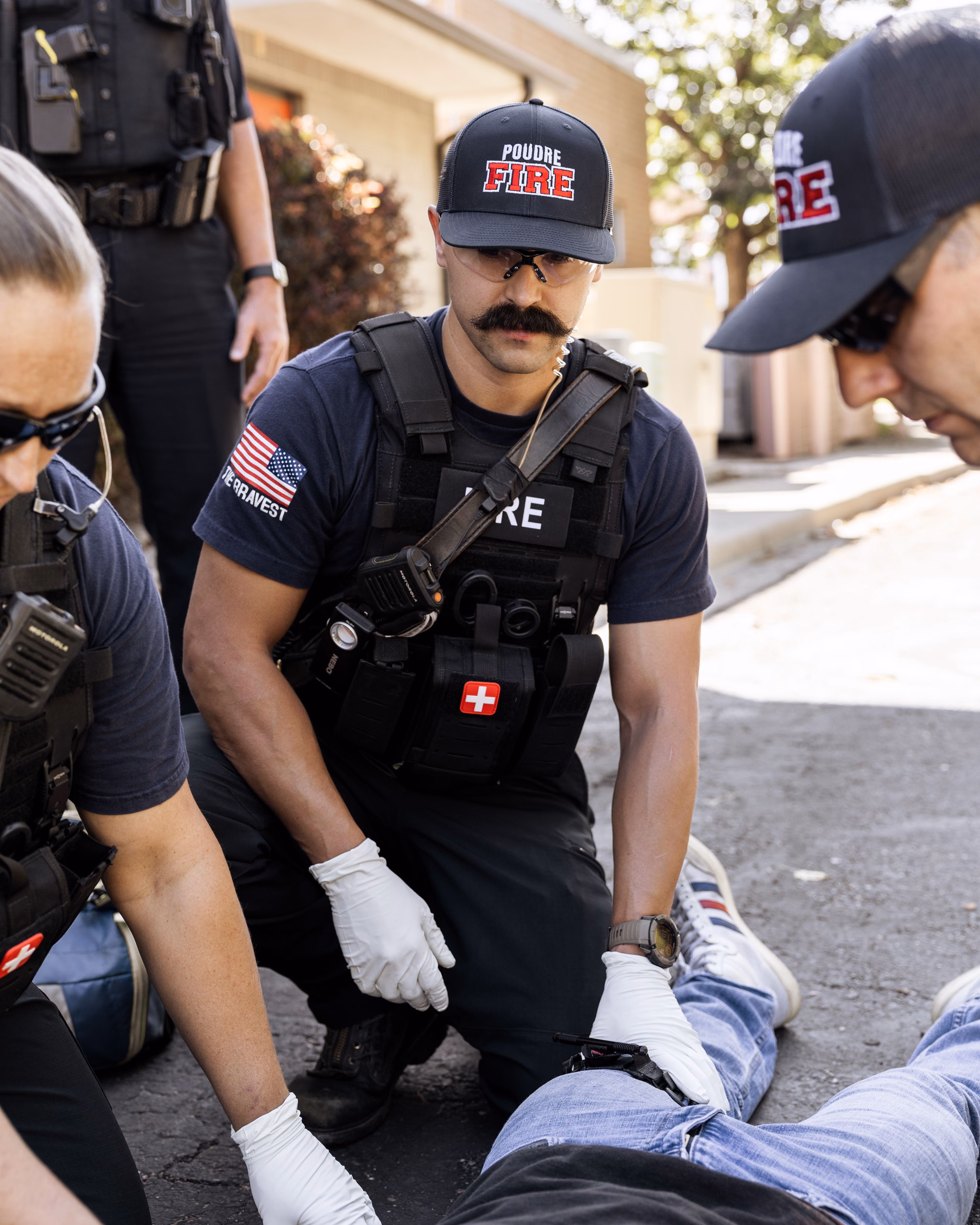 Fire rescue personnel wearing gloves assist an injured person lying on the ground outdoors.