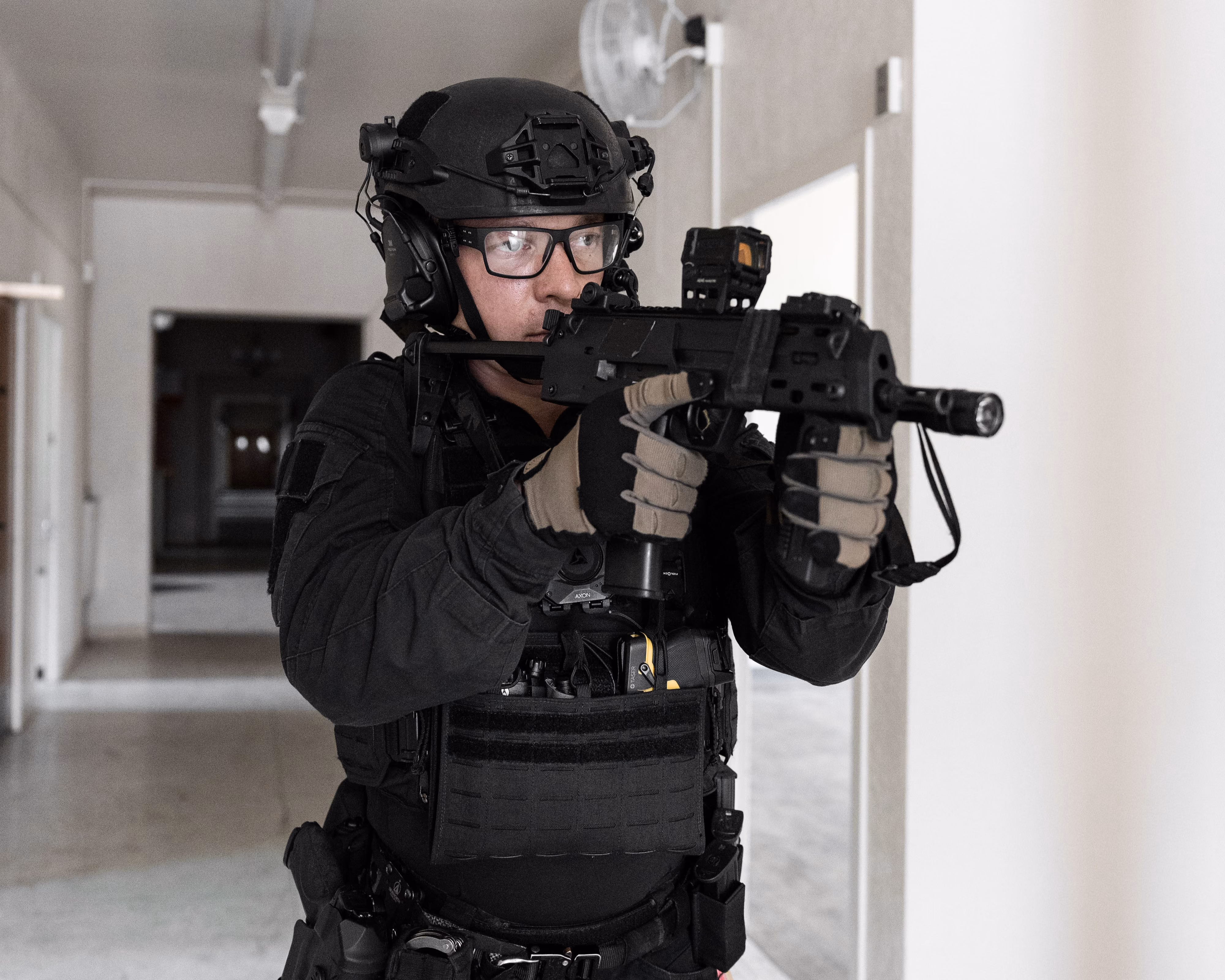 A soldier in camouflage uniform holding a tactical helmet and green body armor in low light.