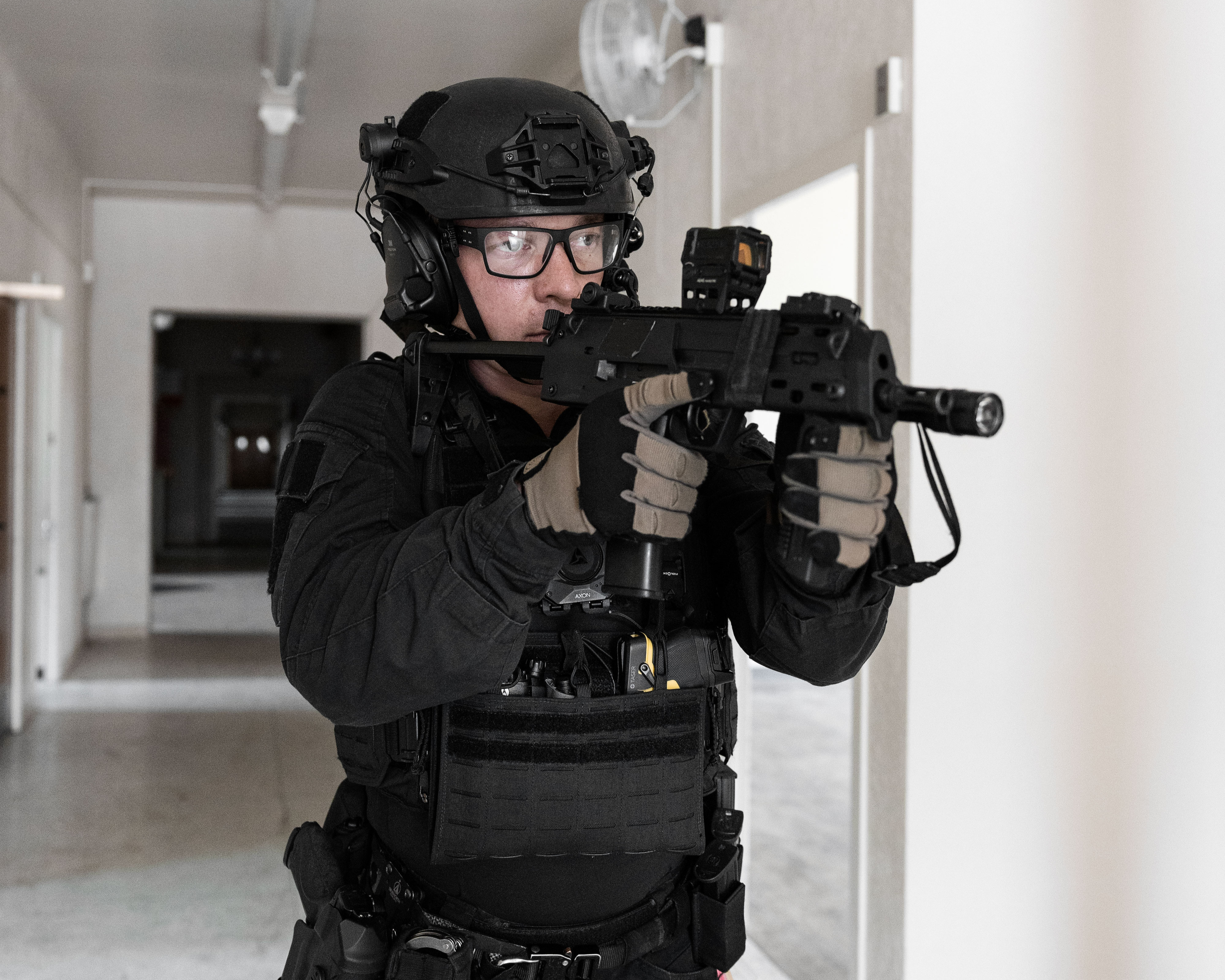 A soldier in camouflage uniform holding a tactical helmet and green body armor in low light.