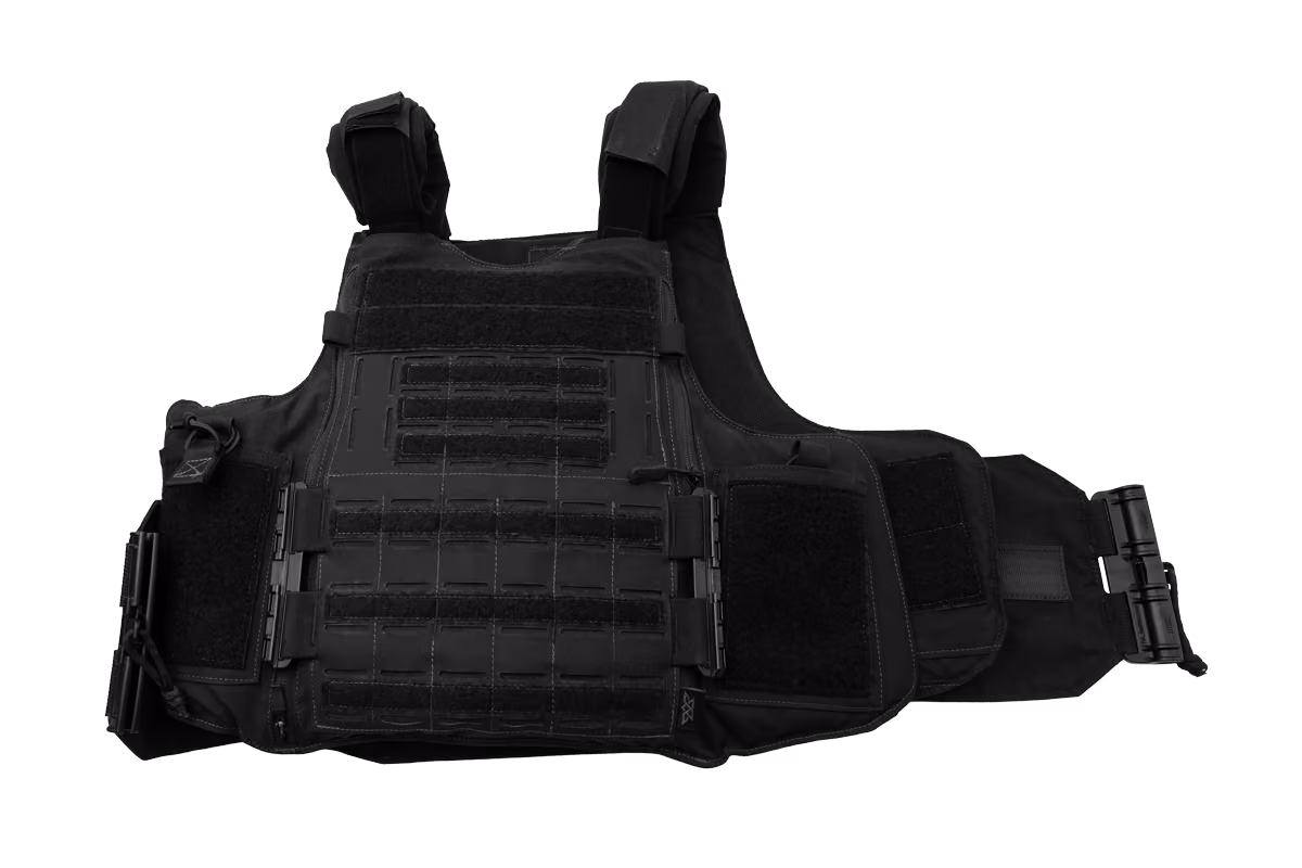 A soldier in camouflage uniform holding a tactical helmet and green body armor in low light.