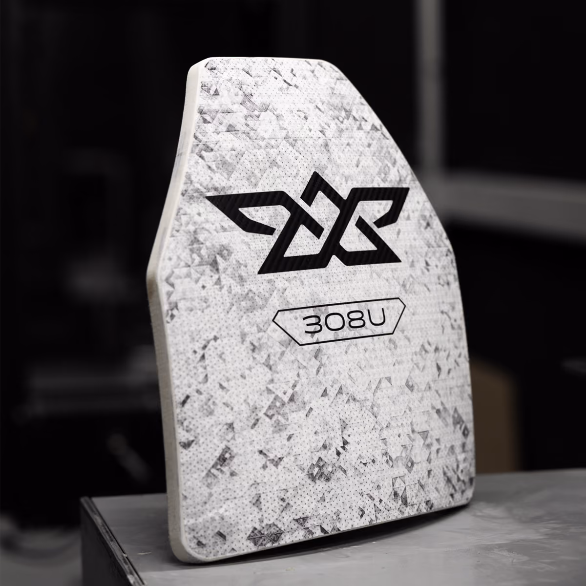 White textured protective armor plate with black geometric logo and text 308U on a gray surface.