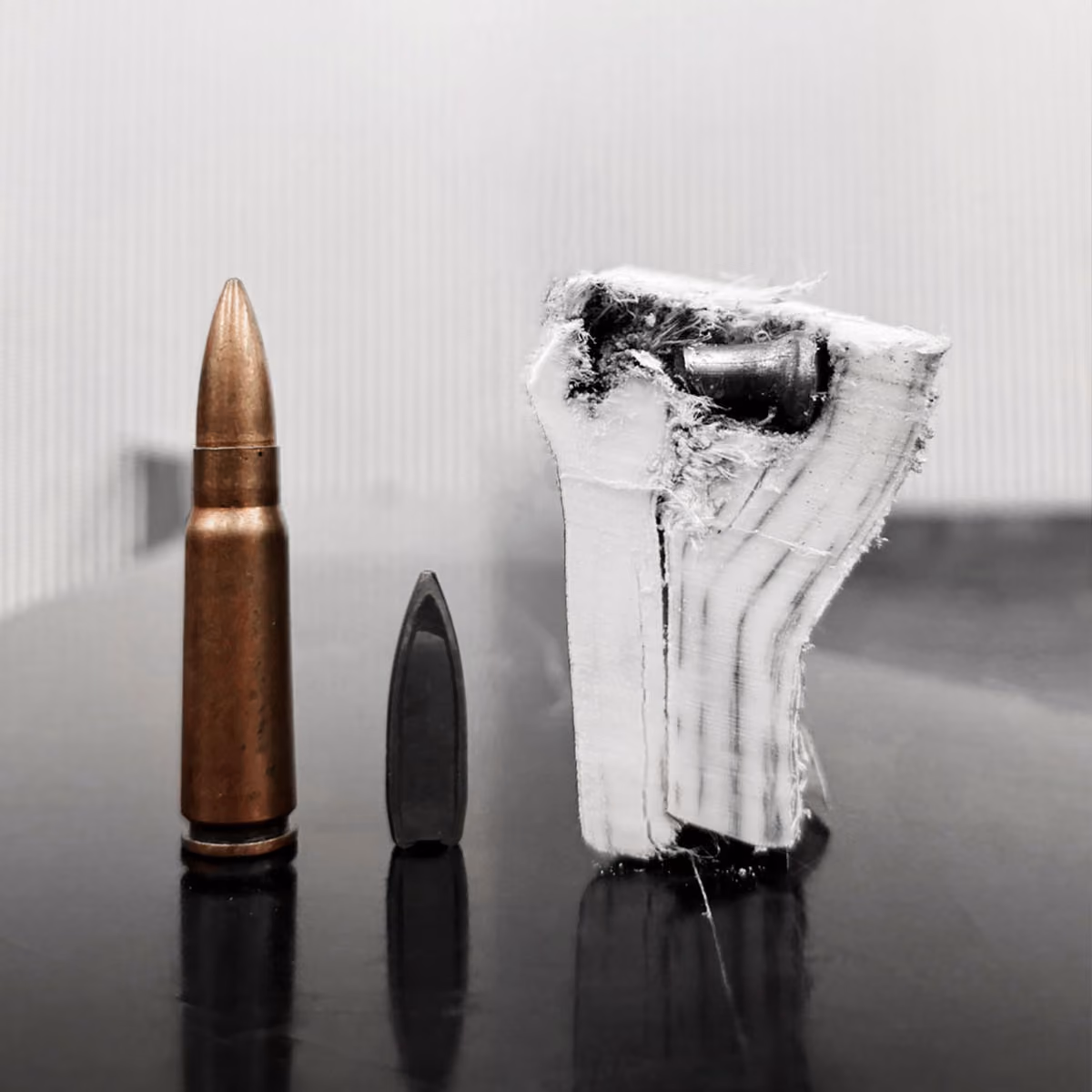 Bullet, bullet tip, and a wooden block with a bullet embedded, shown on a reflective surface.