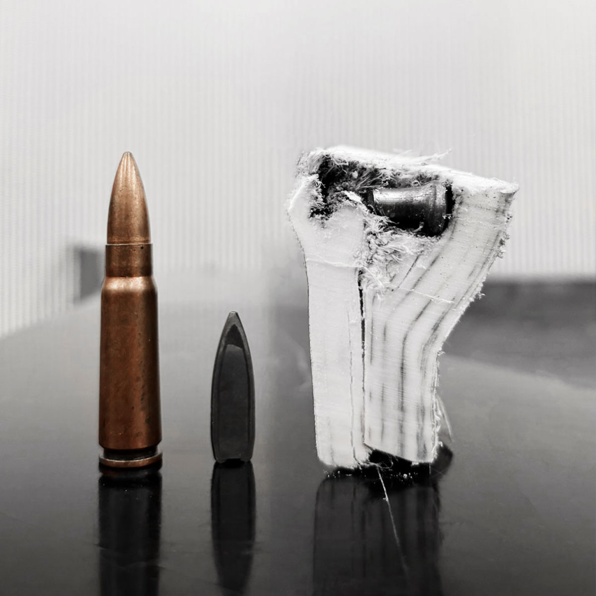 Bullet, bullet tip, and a wooden block with a bullet embedded, shown on a reflective surface.