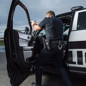 Police officer aiming a handgun while taking cover behind an open patrol car door.