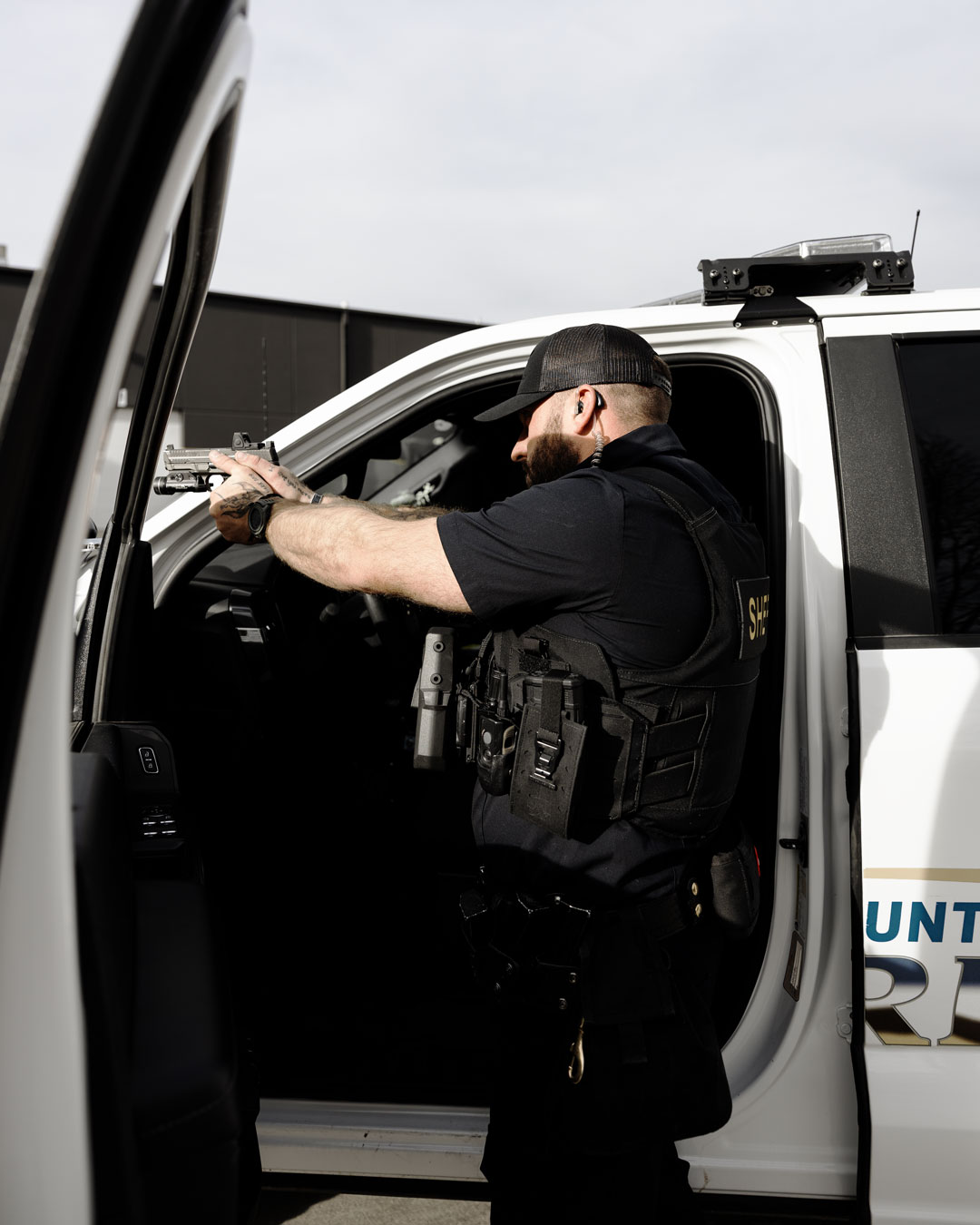Law enforcement officer aiming handgun while standing outside a white police vehicle.