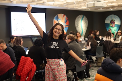 Bri Caplan smiling and wearing a Code Your Dreams shirt, with her arms outspread