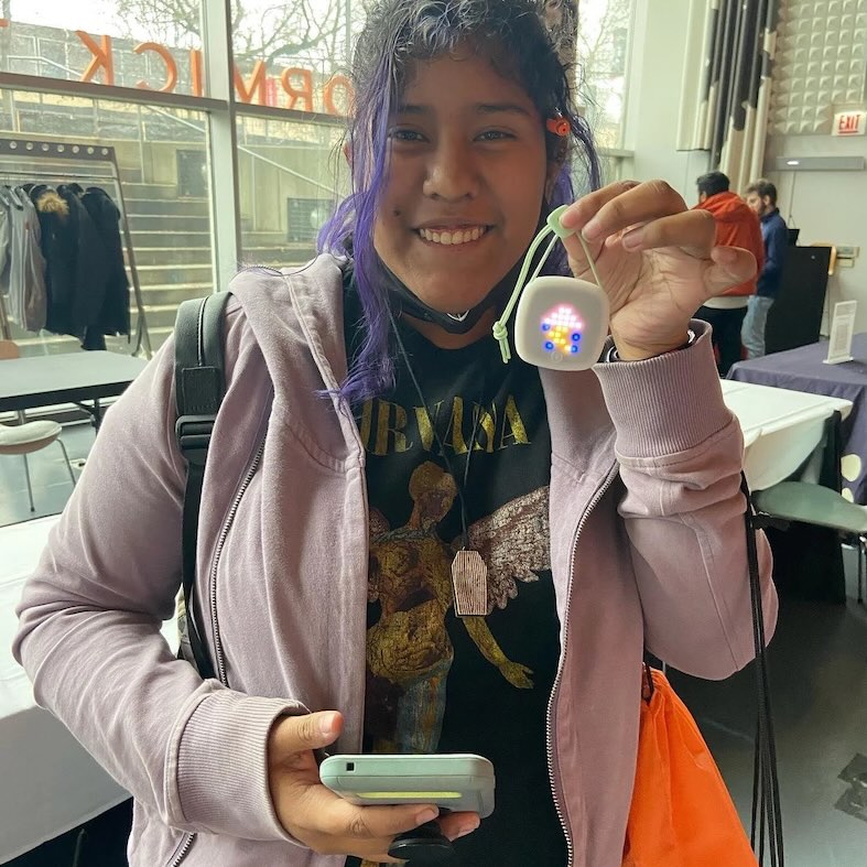 A proud student holding up a small device with glowing LEDs
