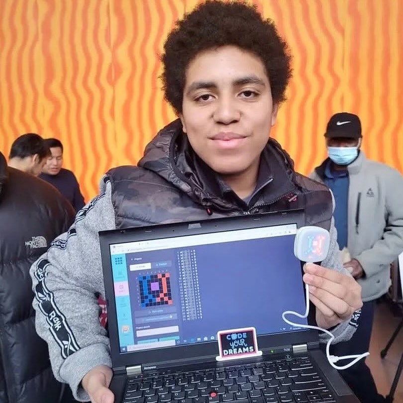 A smiling student displaying a laptop screen and LED device