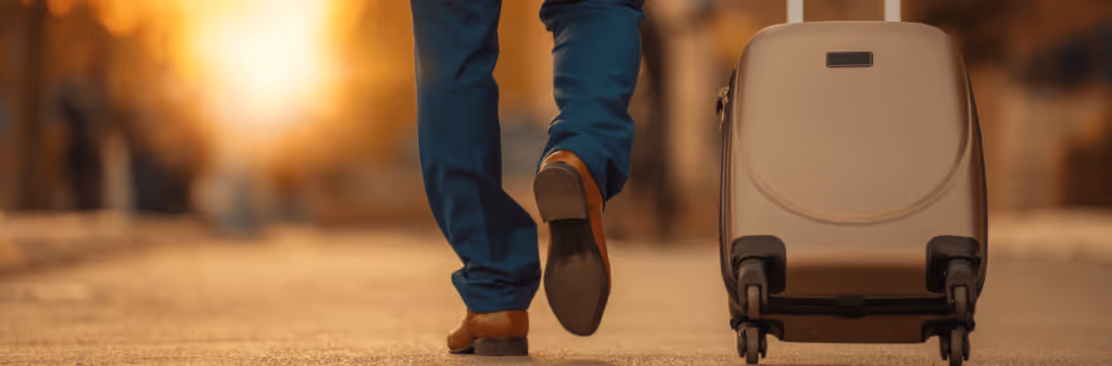 Person walking away on a street, pulling a suitcase with warm sunlight in the background.