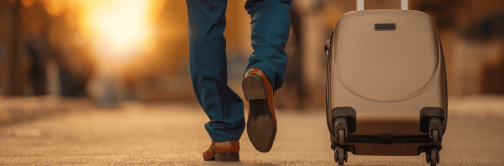 Person walking away on a street, pulling a suitcase with warm sunlight in the background.