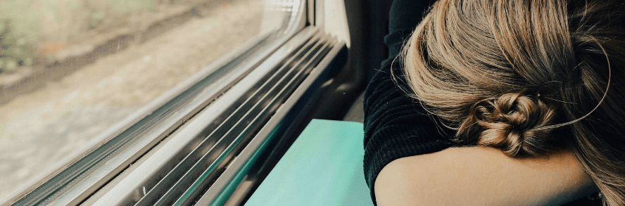A tired person resting their head on folded arms beside a window, symbolizing exhaustion and burnout often experienced during frequent business travel.